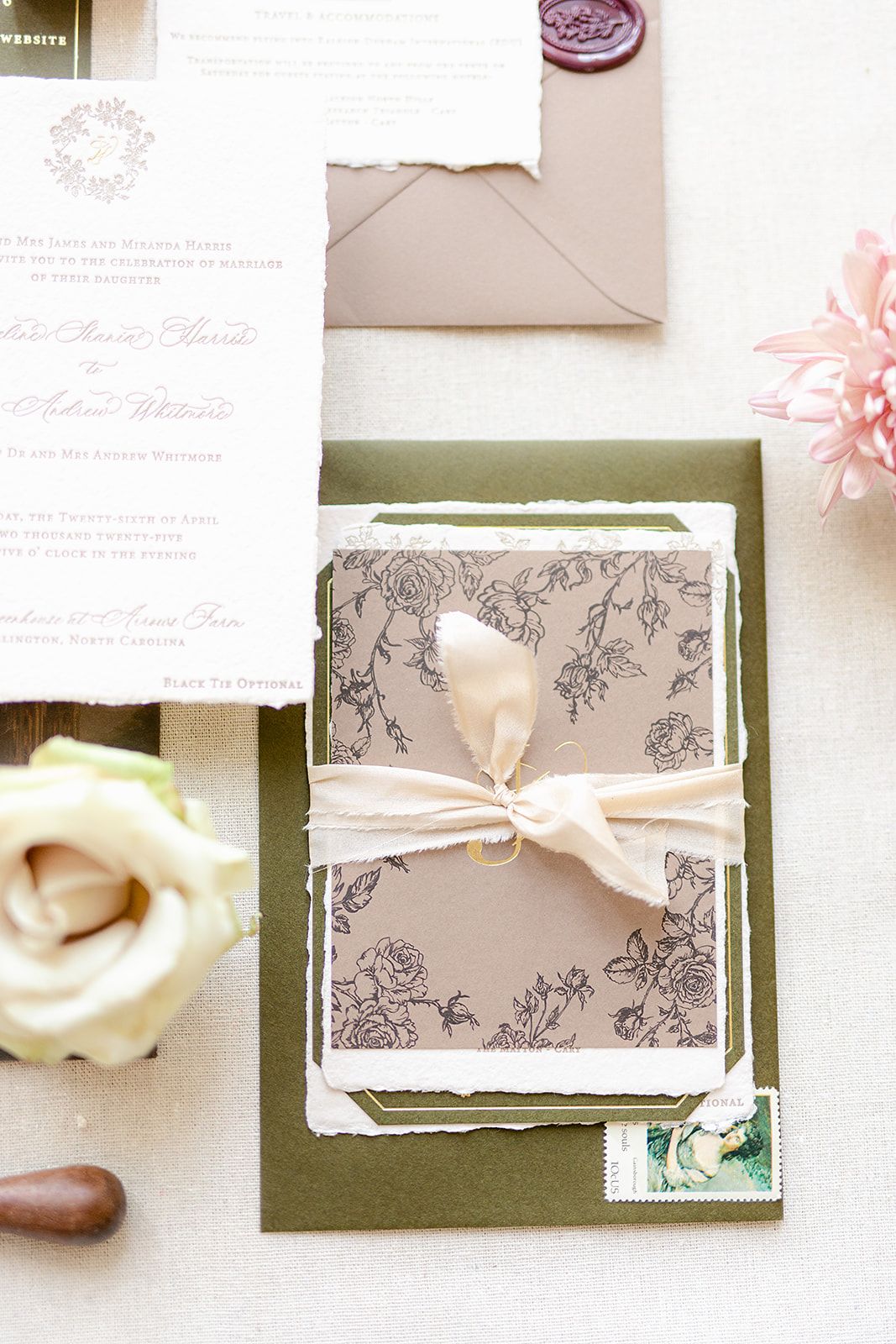 Elegant wedding invitation suite with floral designs in gray and white tones displayed on a green background.