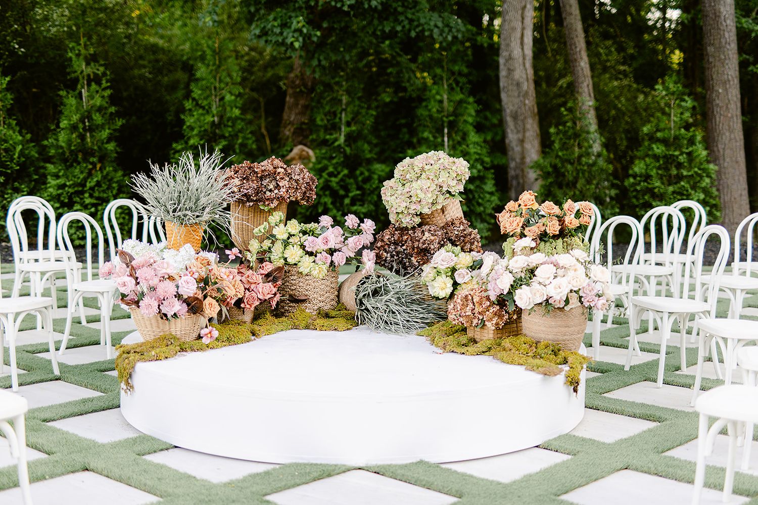 White chairs arranged in rows for an outdoor garden wedding ceremony with floral decorations and greenery.