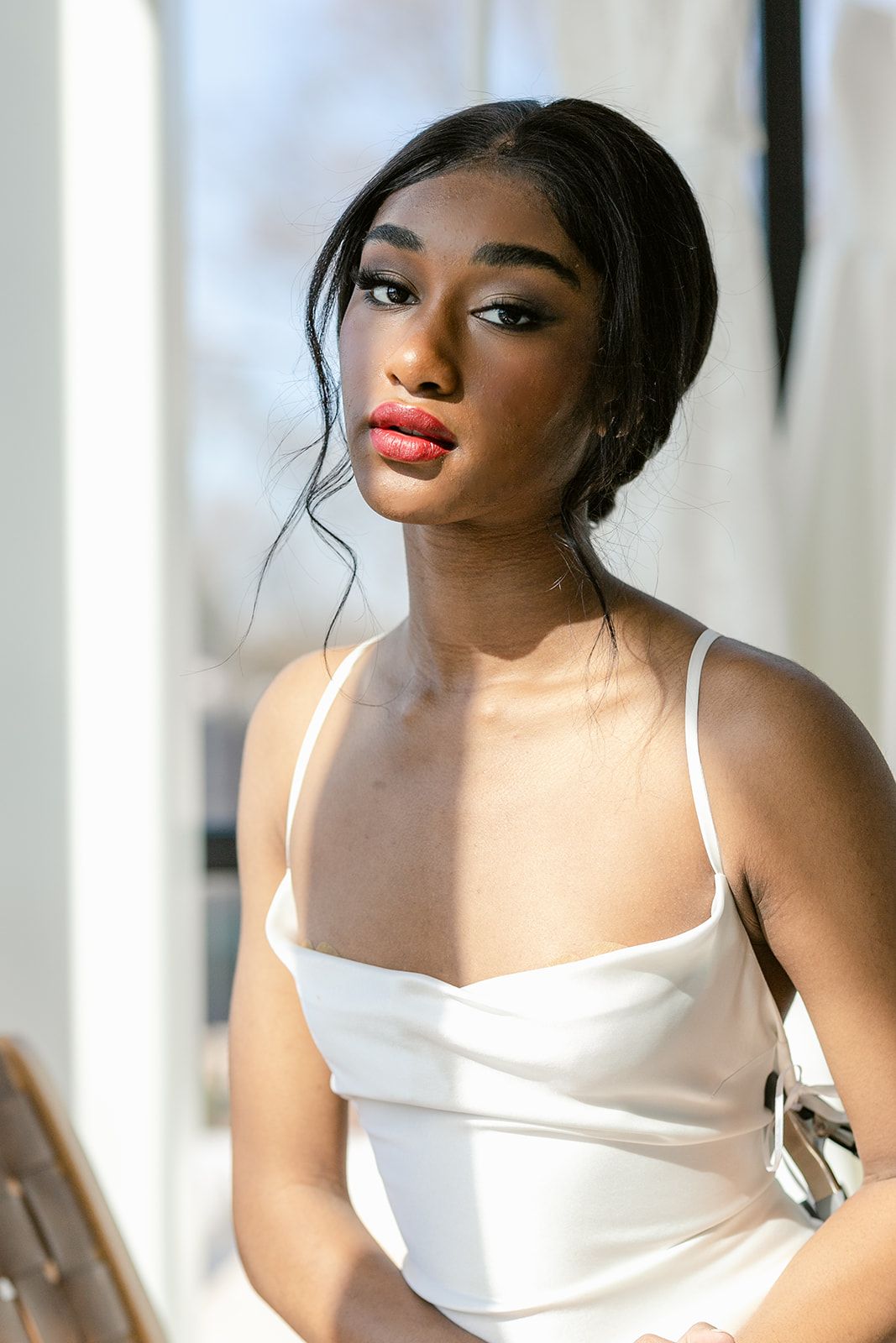Woman in white spaghetti strap top poses elegantly against bright interior background.