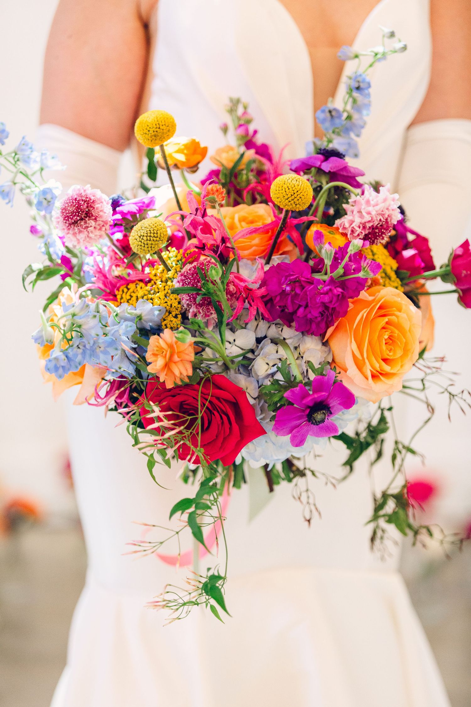 Vibrant bridal bouquet featuring orange roses, pink dahlias, and purple wildflowers.
