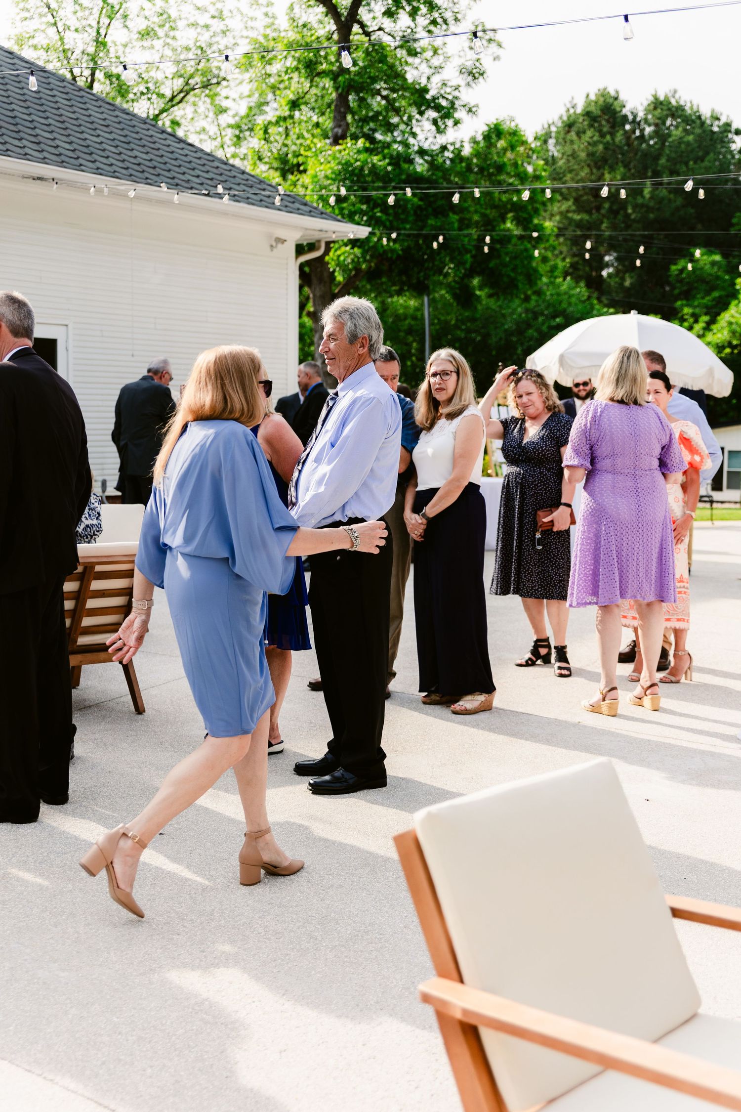 Wedding guests dance in a line on an outdoor white patio during a celebration.