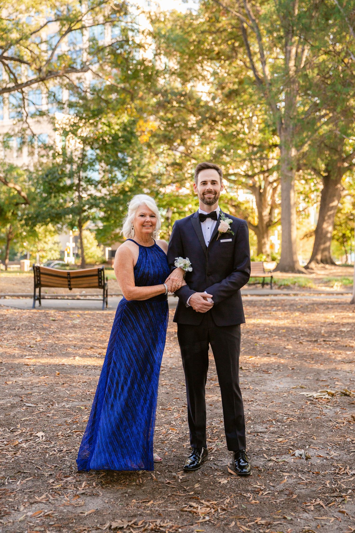 Formal couple poses outdoors in autumn park setting with blue gown and black tuxedo.