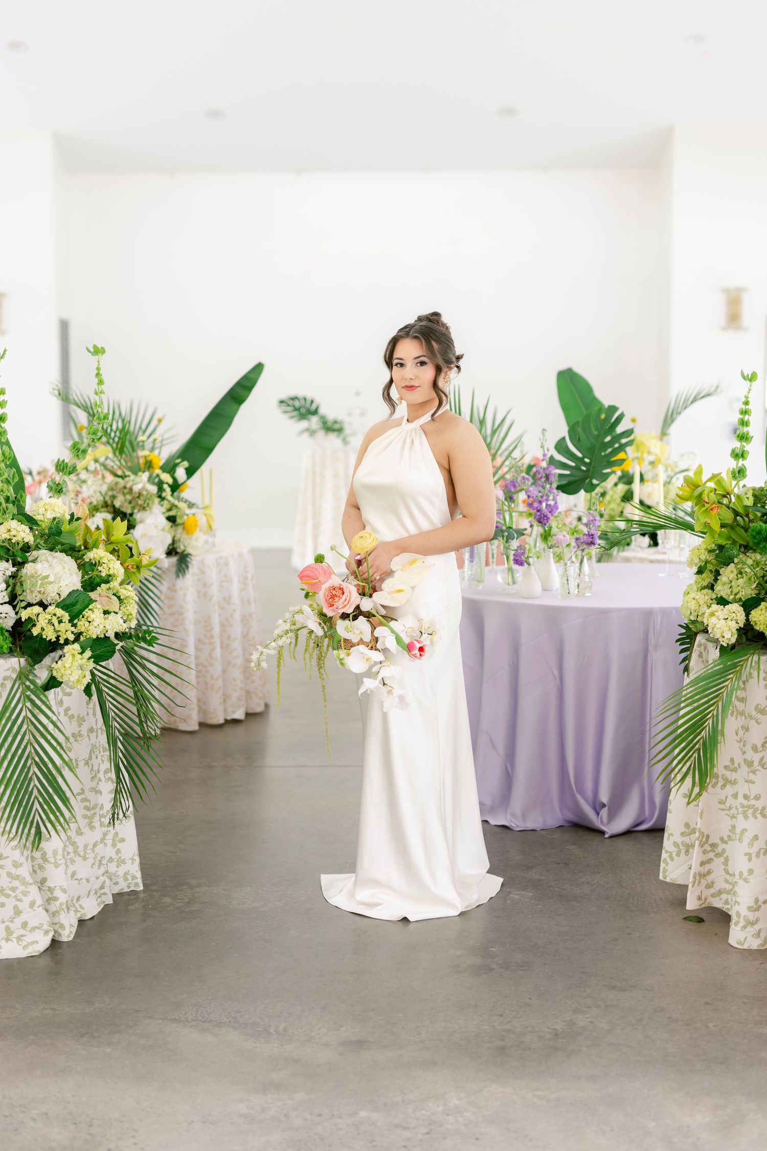 Elegant wedding scene with white gown, tropical greenery and lavender accents in a bright modern venue.
