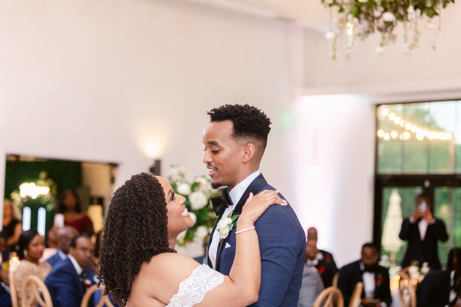 Wedding guests dance and celebrate on a brightly lit dance floor at an elegant indoor reception venue.