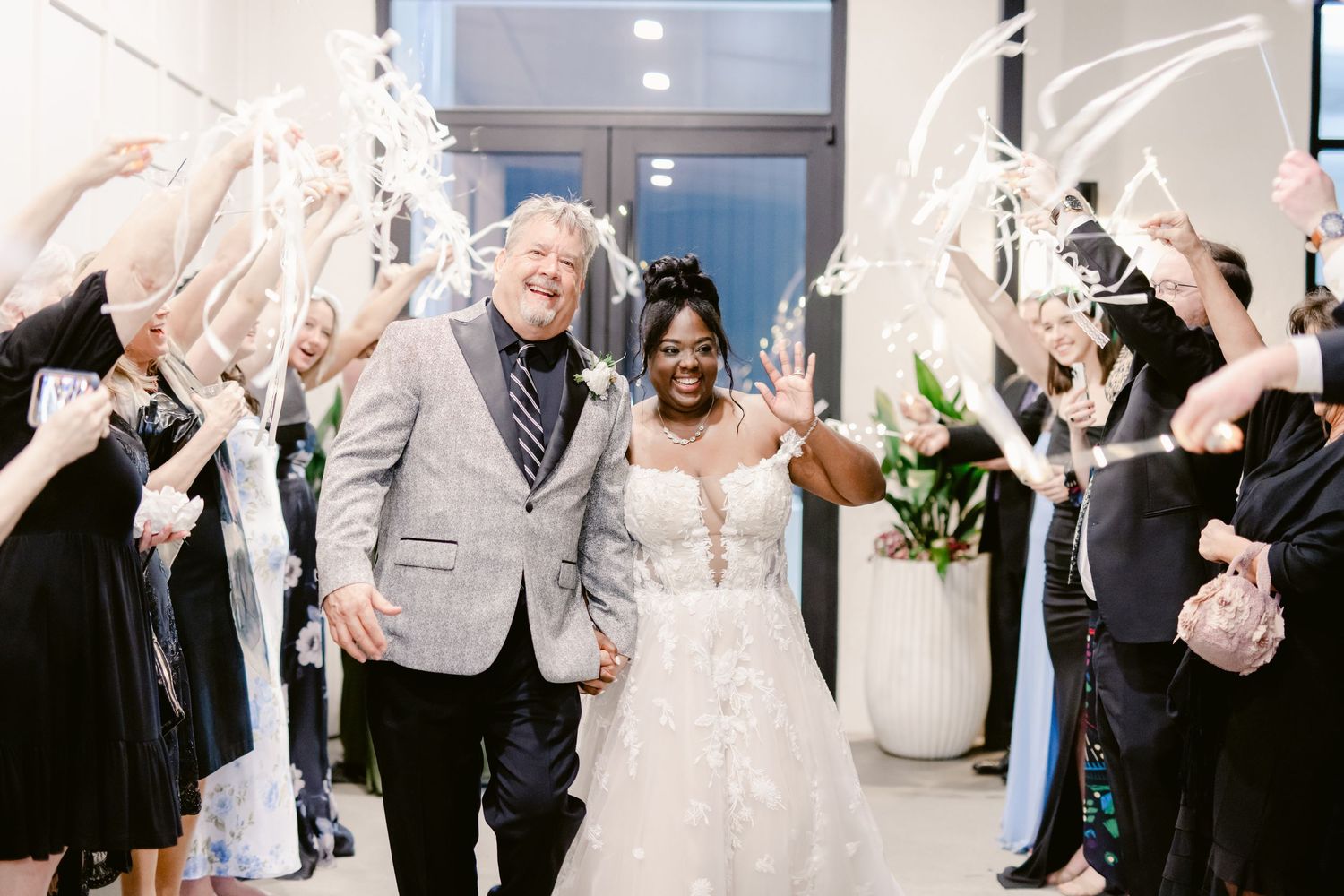 Wedding guests dance and celebrate on the dance floor at an elegant reception venue with white decor and lighting.