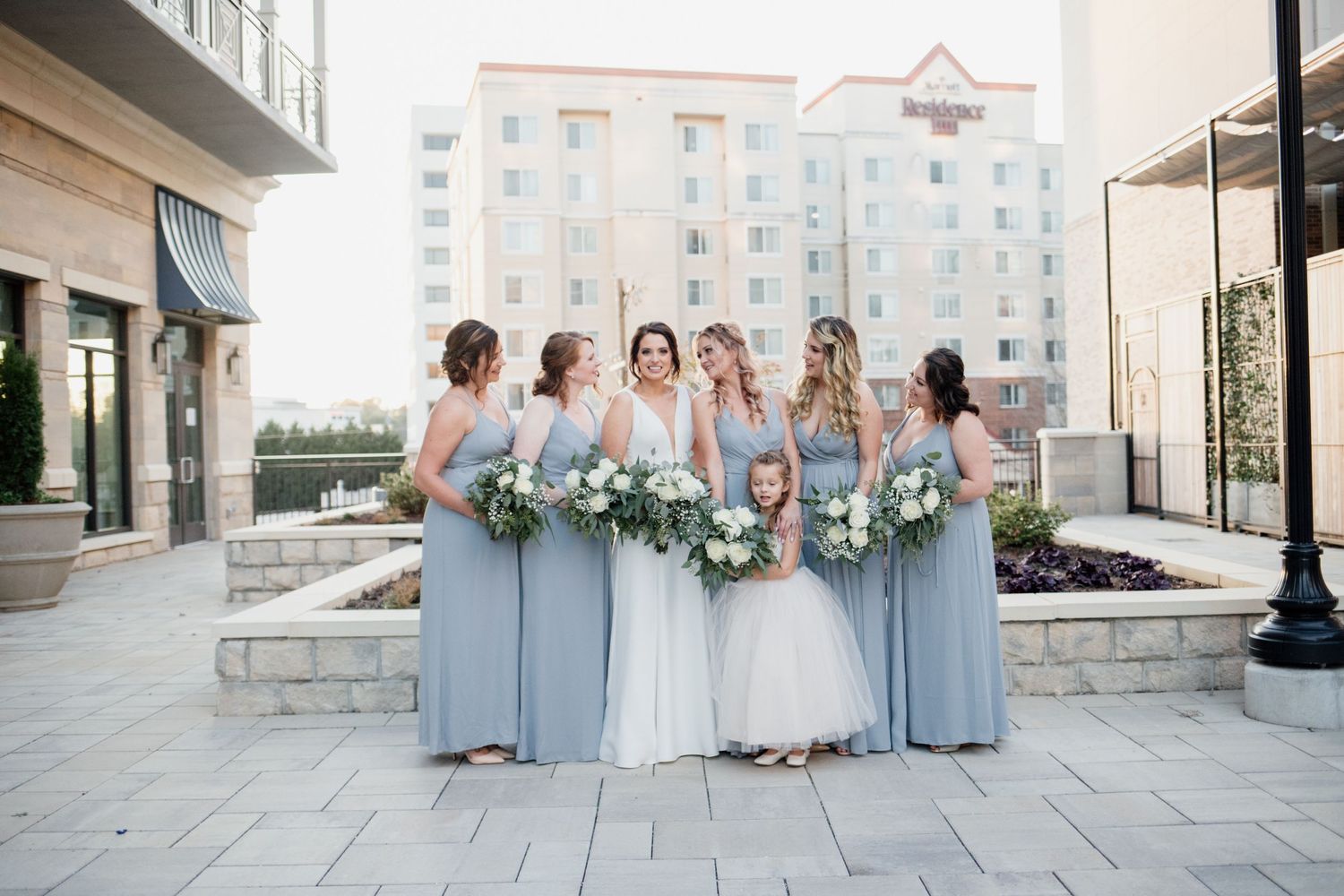 Bridesmaids in light blue dresses pose with bride holding white floral bouquets.