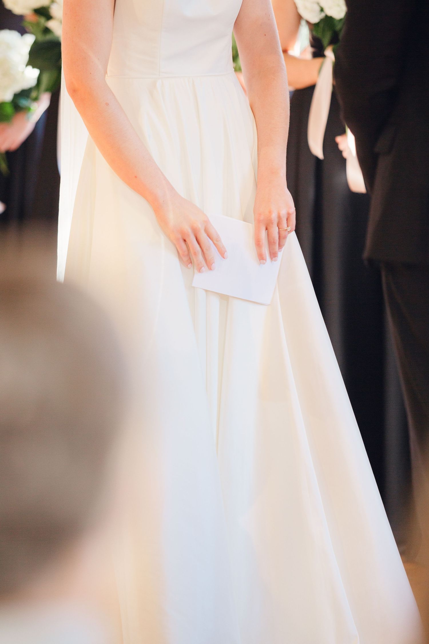 A close-up view of a white wedding dress and hands holding a paper during a ceremony.