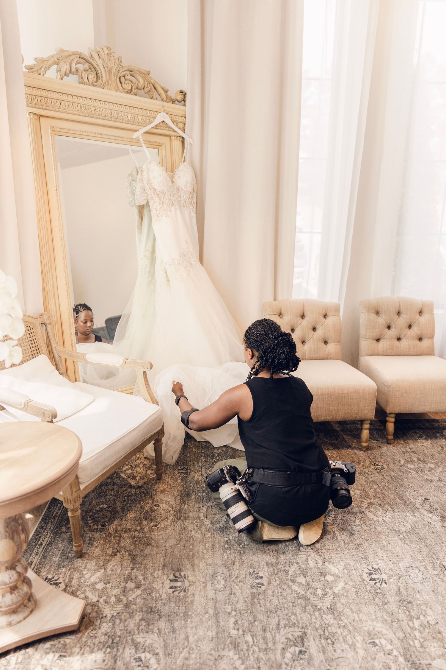 Behind-the-scenes photographer capturing wedding dress details in an elegant room with ornate furniture and decor.