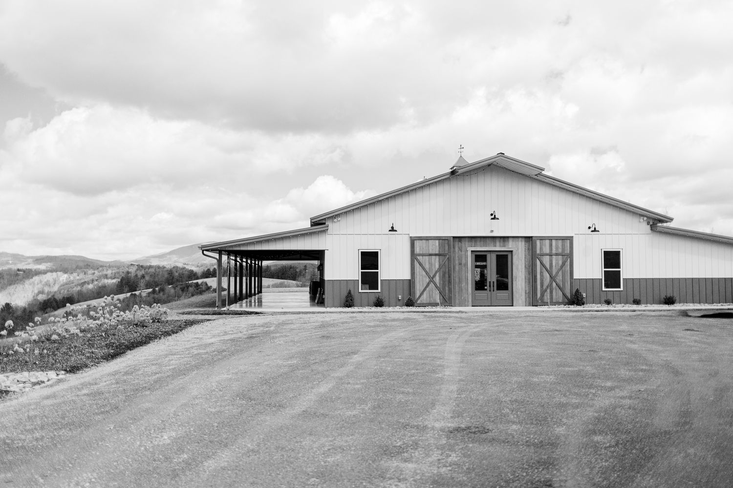 A long row of modern industrial buildings with metal siding extends across a rural landscape under cloudy skies.