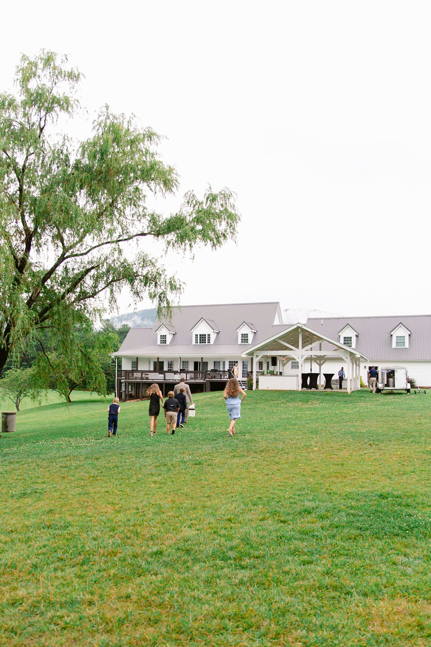 Scenic view of a white farmhouse with dormer windows set on a green hillside lawn.