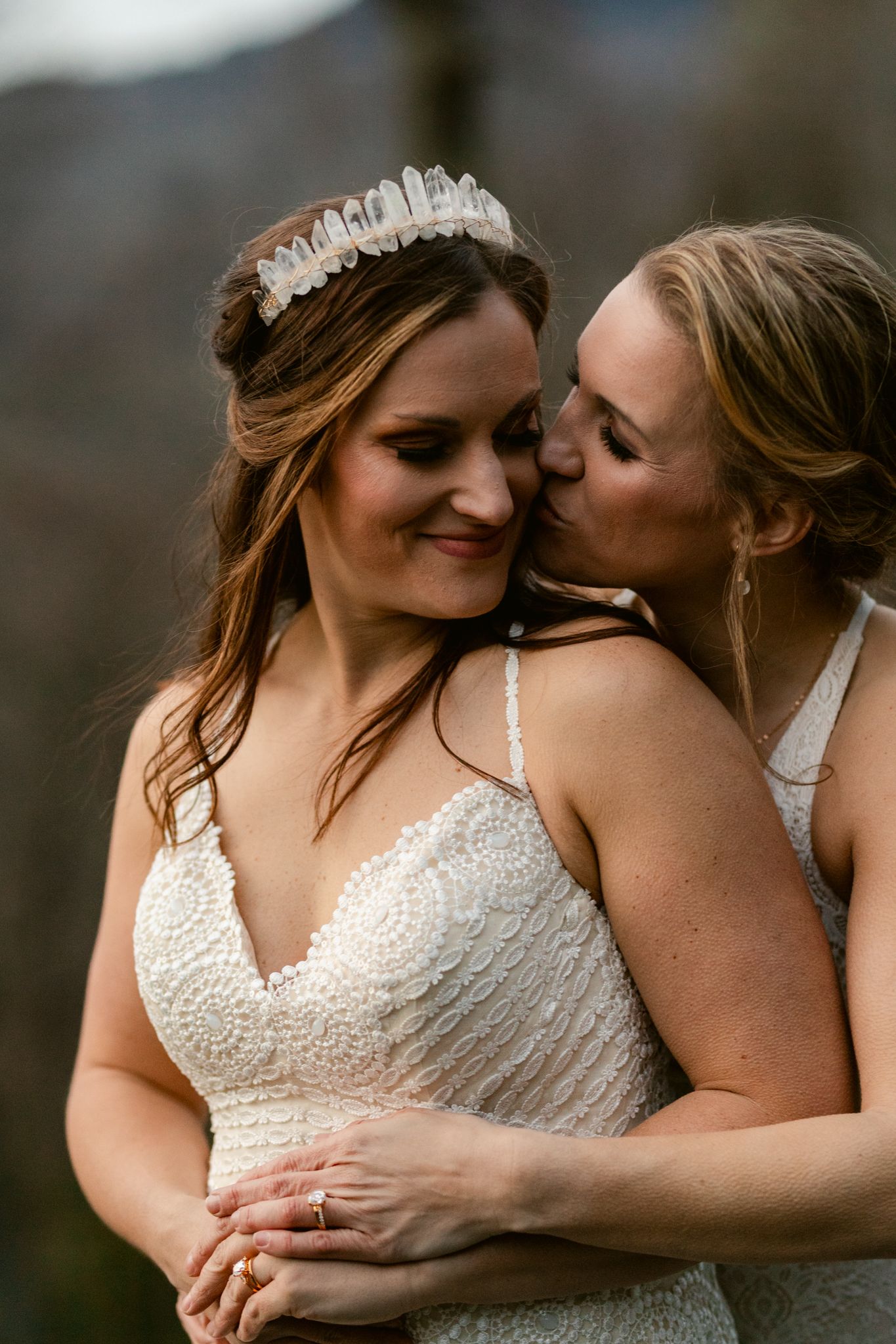 A romantic moment captured between two people in white beaded wedding dresses against a mountain setting.