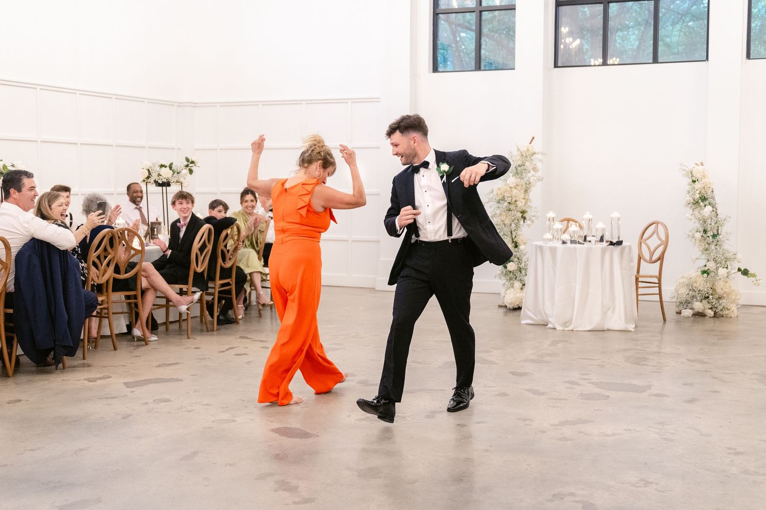 Wedding guests dancing in formal attire at an elegant white reception venue.