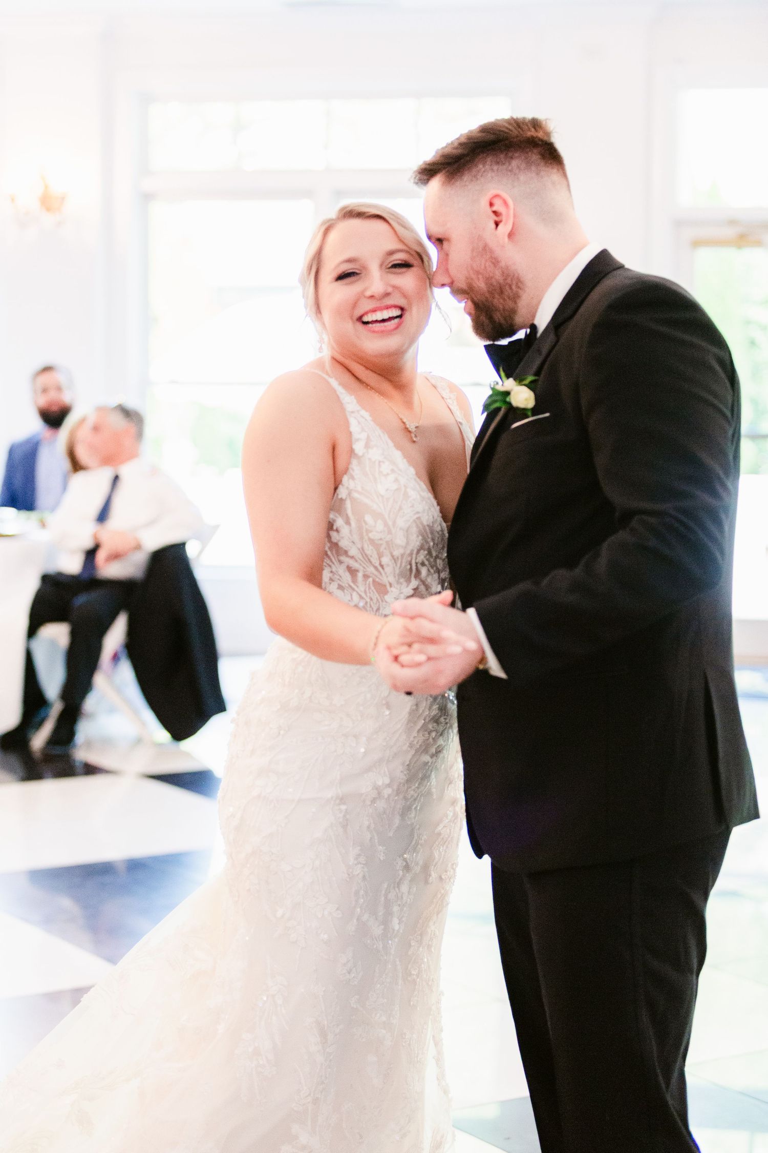 A bride and groom share a joyful dance together during their wedding celebration in a bright indoor venue.