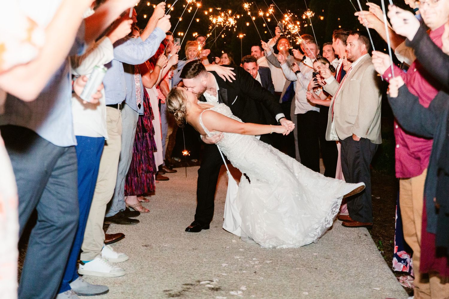 Wedding guests form a circle on the dance floor during a reception celebration with twinkling lights overhead.