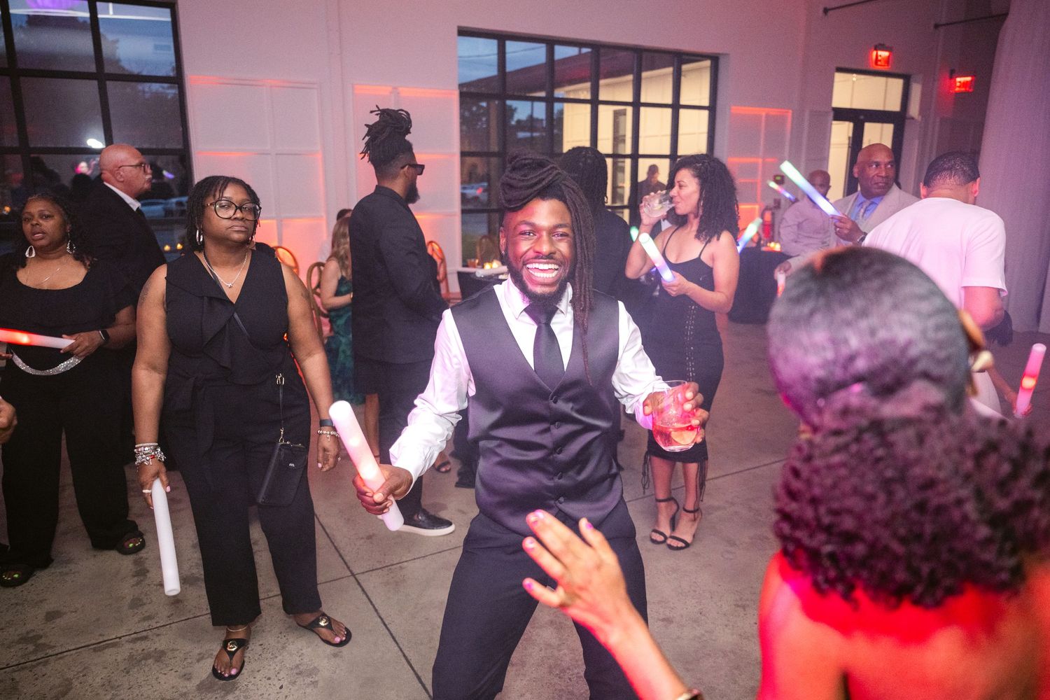 Wedding reception dance floor with guests dancing under pink mood lighting.