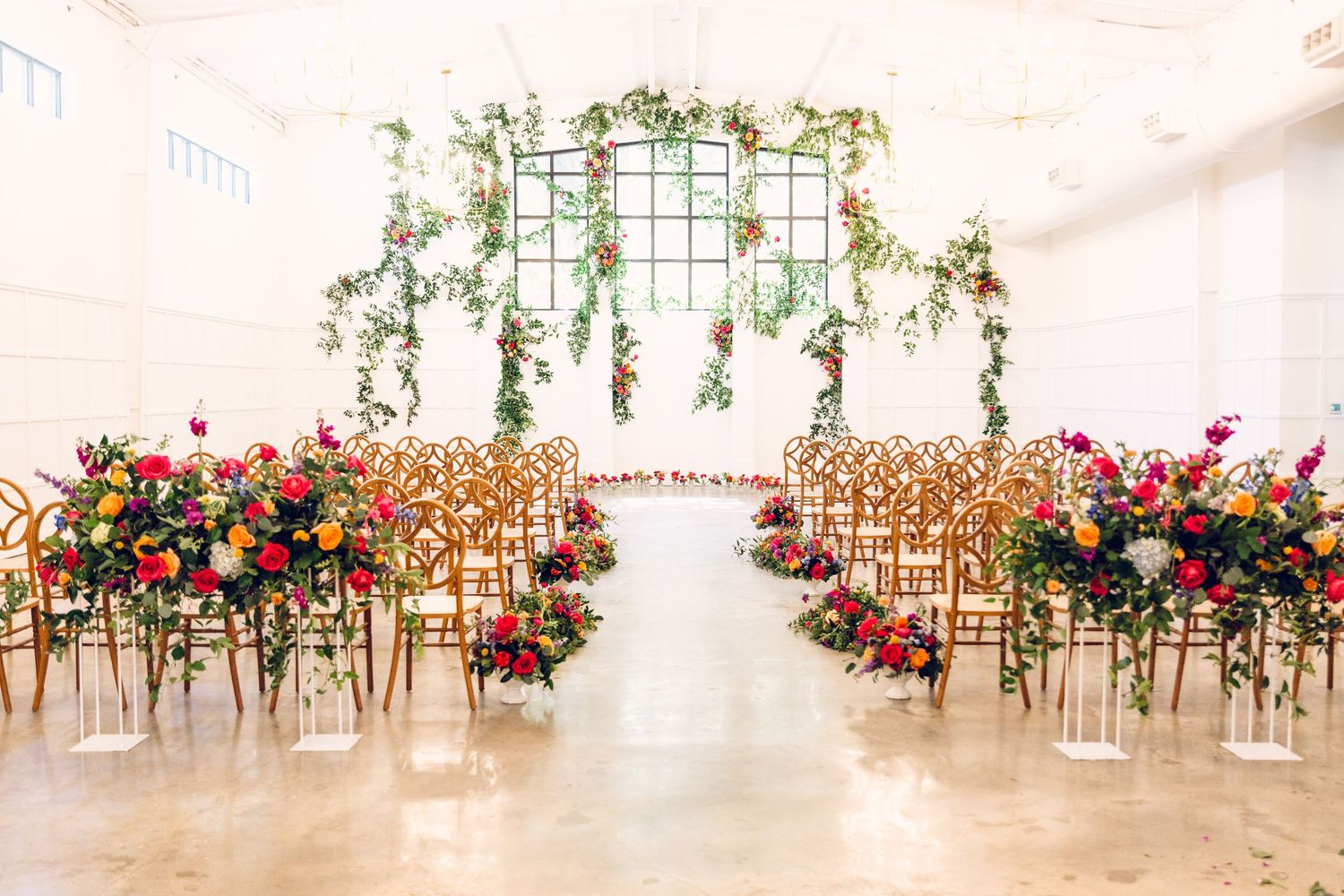 Modern wedding venue decorated with colorful flowers and wooden chairs in a bright white space.