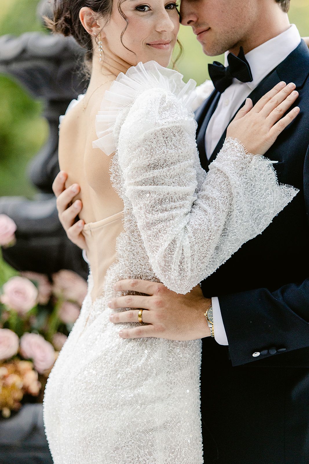 A romantic wedding couple embraces in formal attire, with the bride wearing a sparkling long-sleeved white gown.