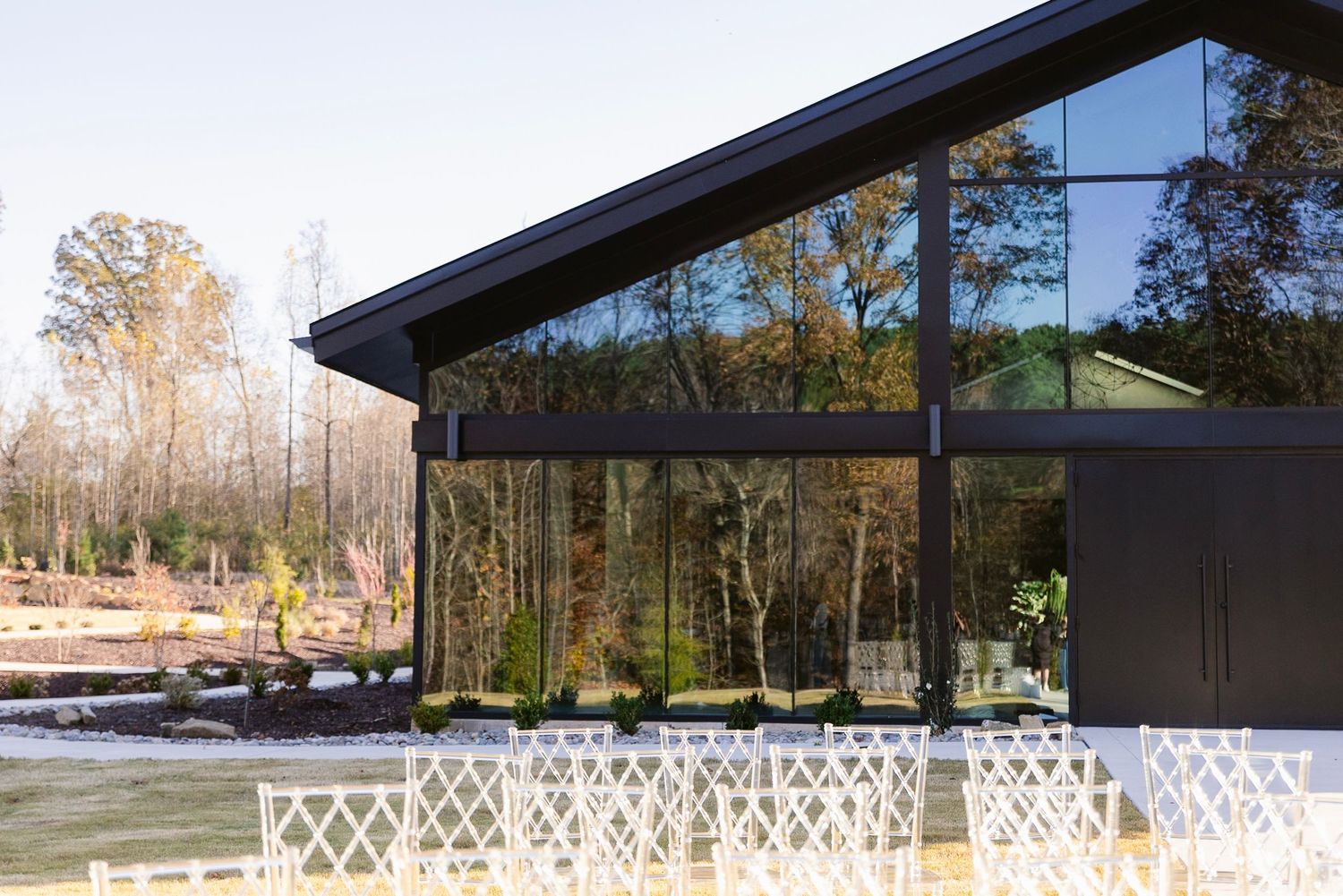 Modern black building with large glass windows and white lattice decorations set against a wooded natural backdrop.