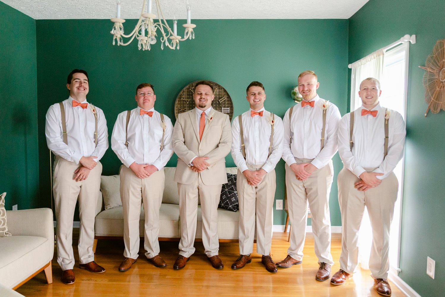 Wedding party in white attire poses against an emerald green wall with a chandelier.