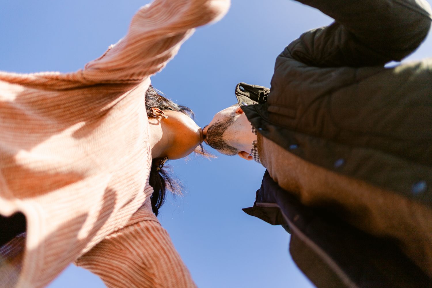A brown horse gallops through a field with its mane flowing in the wind against a blue sky background.