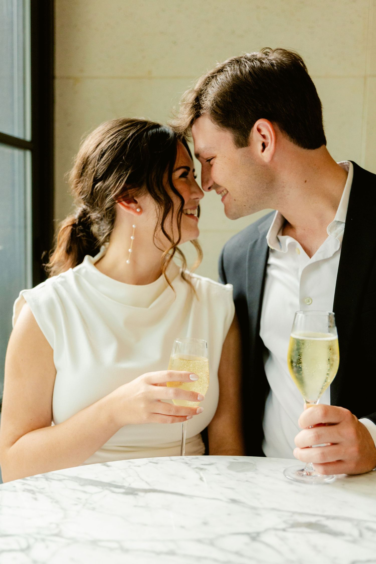 A romantic couple shares an intimate moment while enjoying champagne at a white marble table.