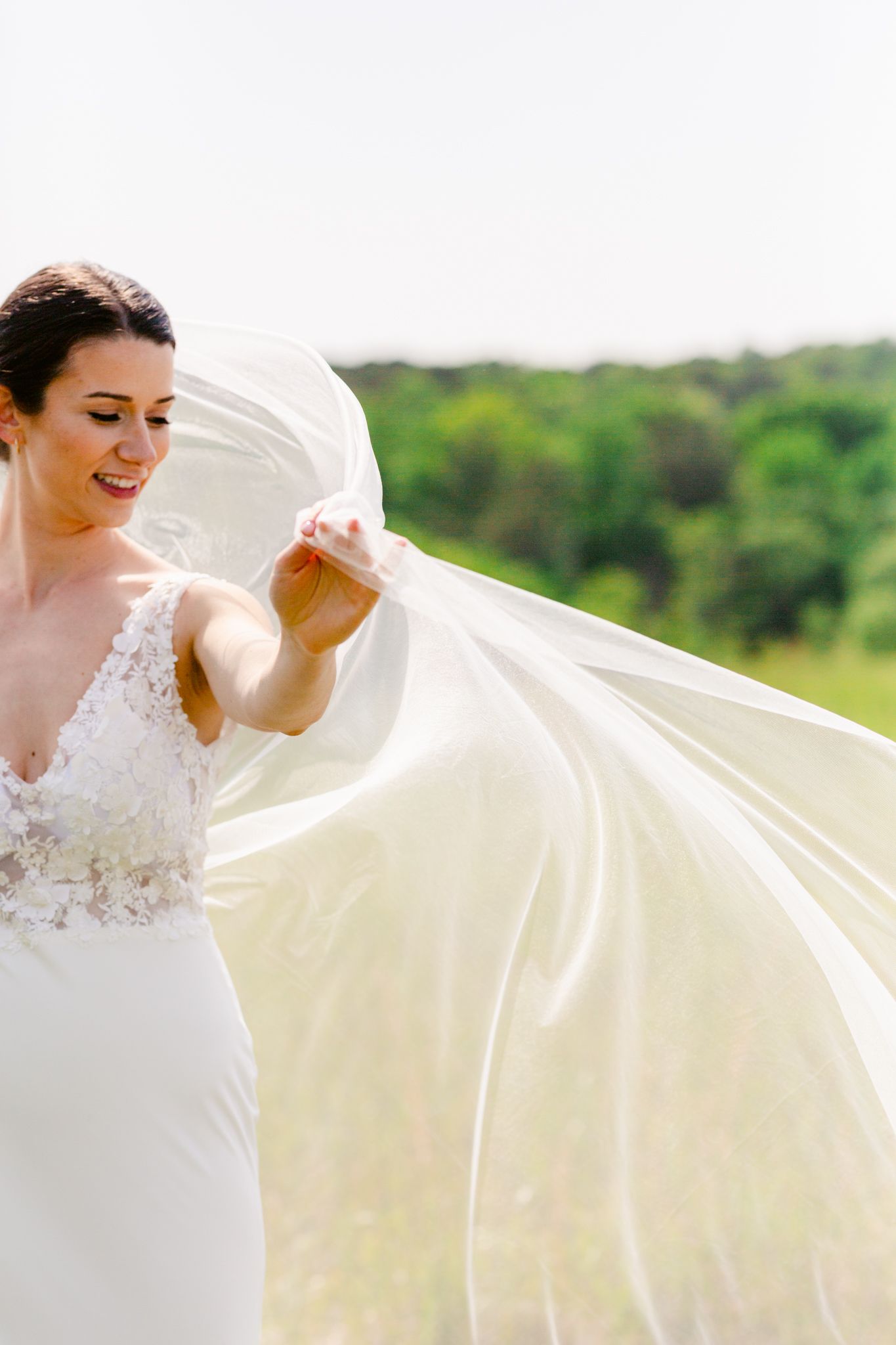 A flowing white wedding veil billows gracefully in the breeze as a bride poses in an outdoor setting.