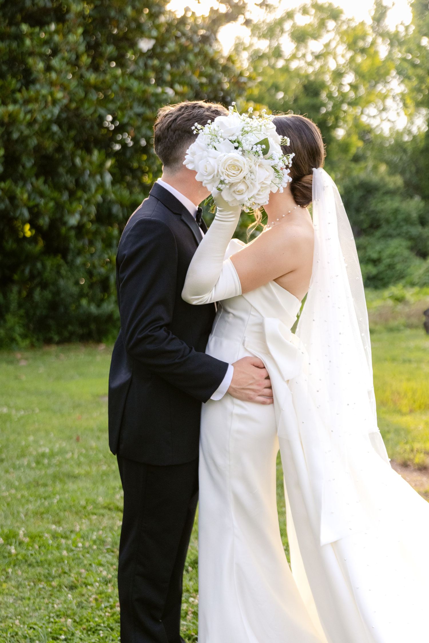 A romantic wedding moment captured at sunset with a white bridal bouquet held between the couple.