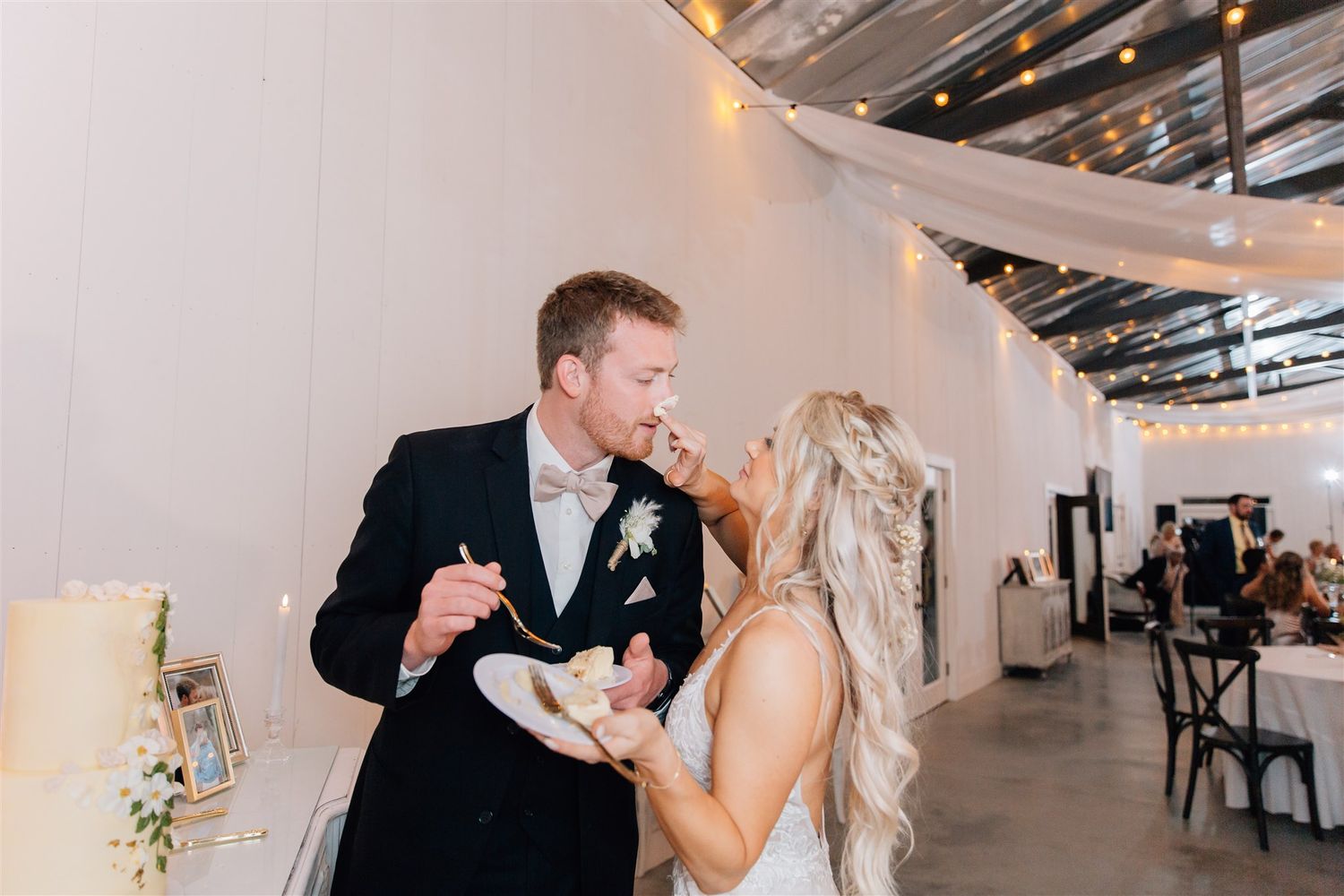 Couple shares cake during reception in modern white industrial venue.
