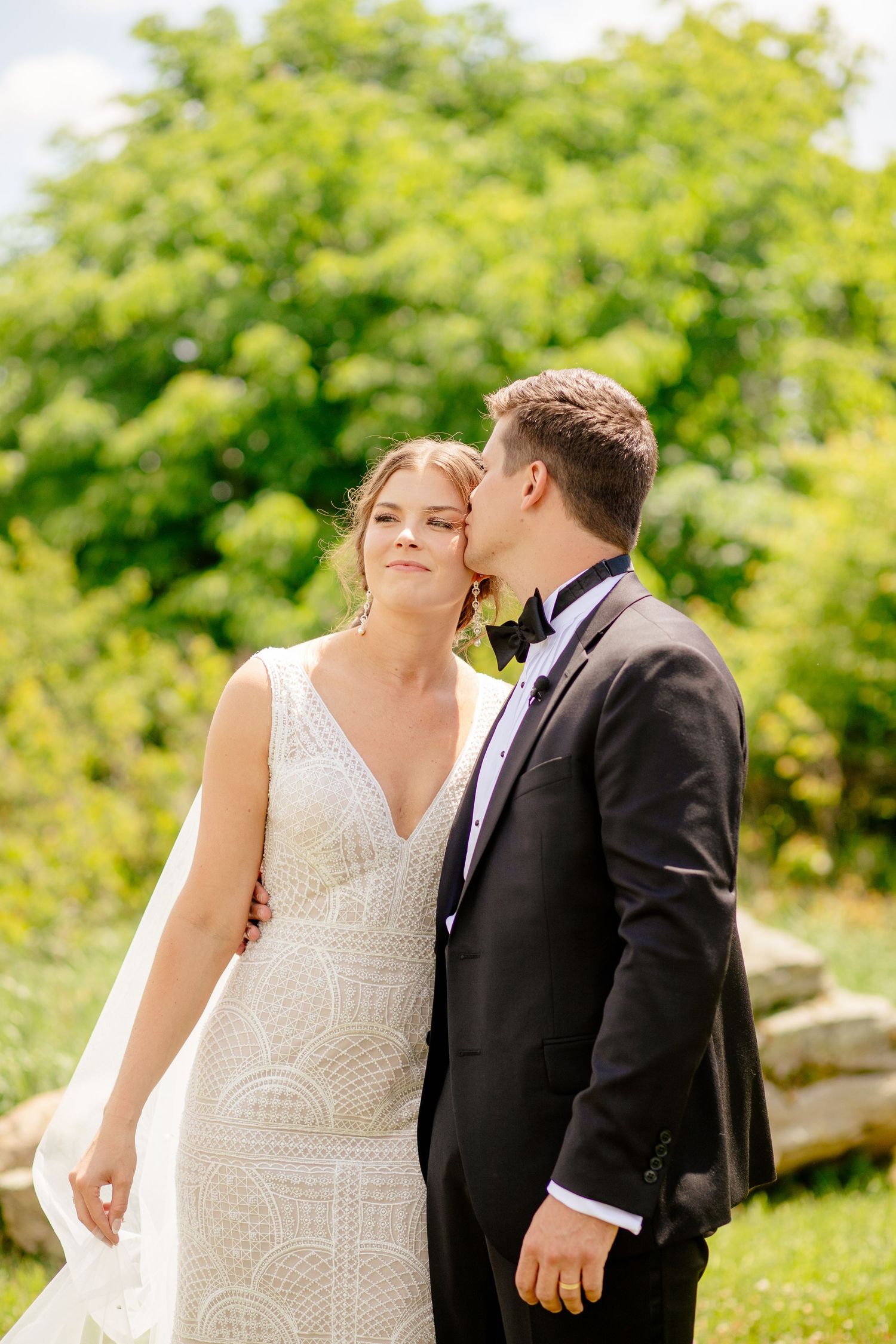 An intimate moment between newlyweds in a garden setting with the bride wearing a detailed lace gown.