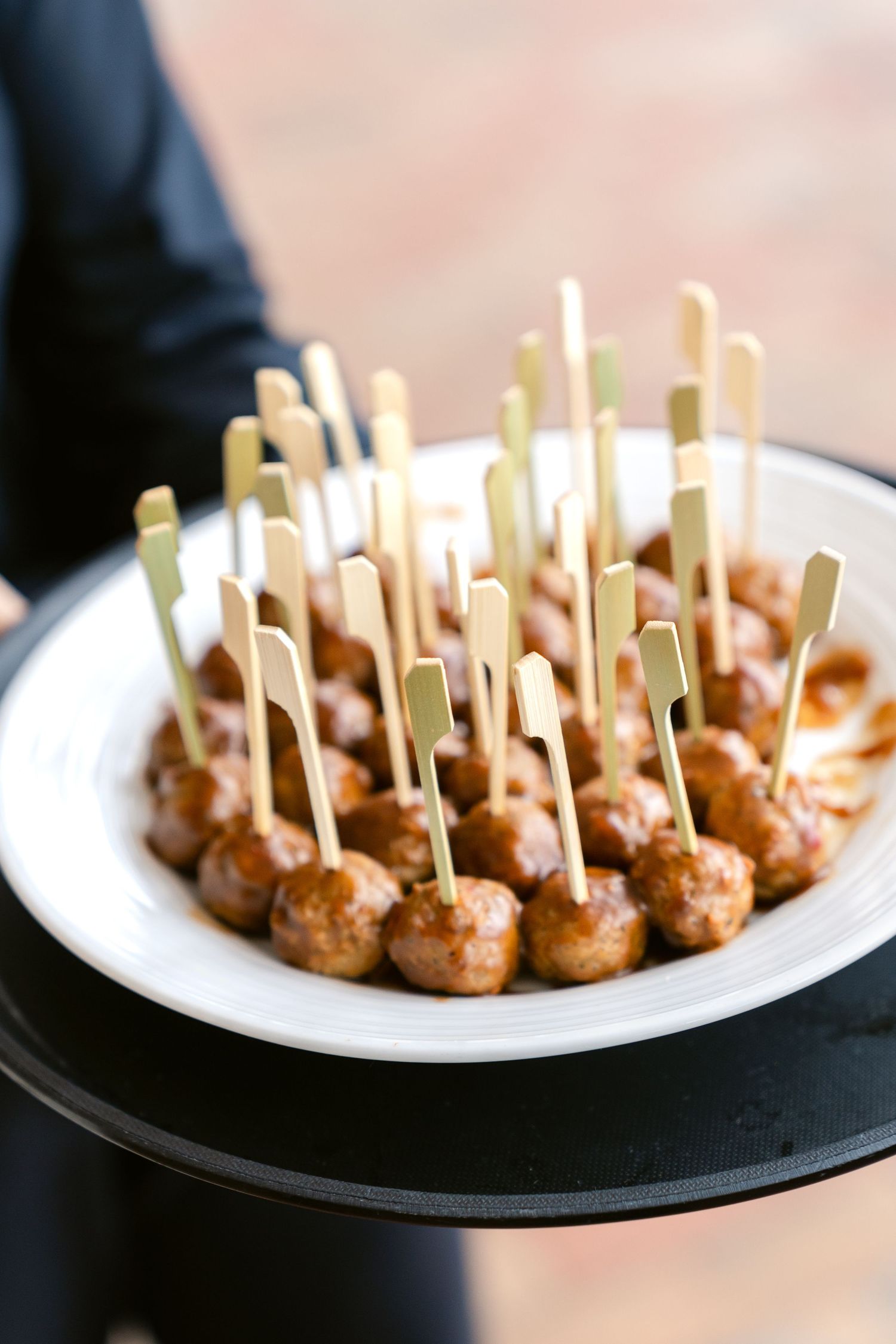 Appetizer plate featuring golden brown meatballs with decorative toothpicks served on white dishes.