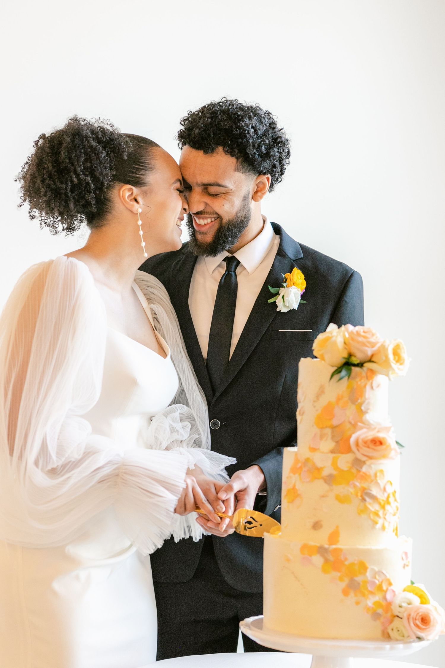 A couple shares an intimate moment near an elegant orange watercolor wedding cake with delicate floral details.