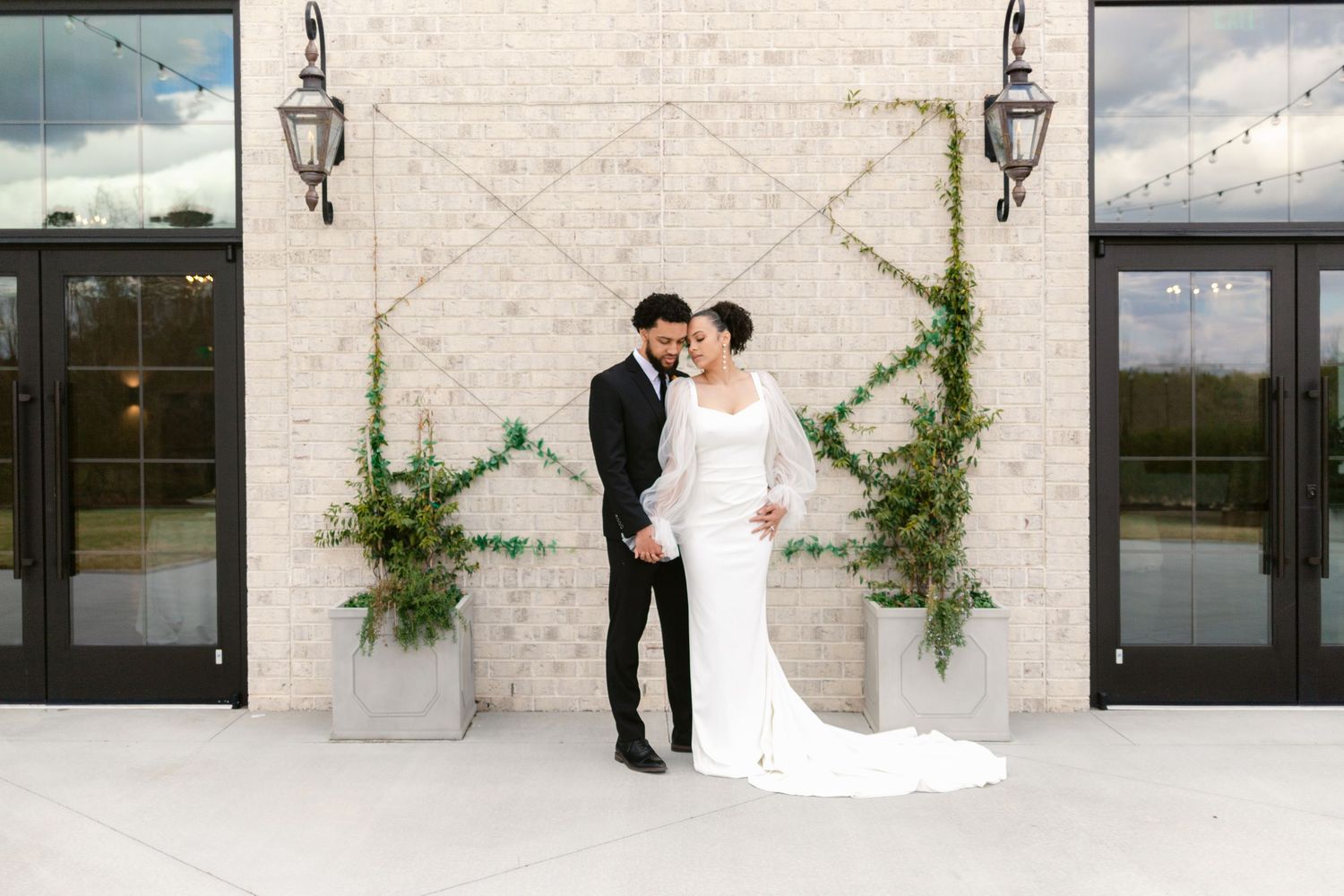 Wedding couple shares intimate moments against modern stone wall backdrop with greenery and black doors.