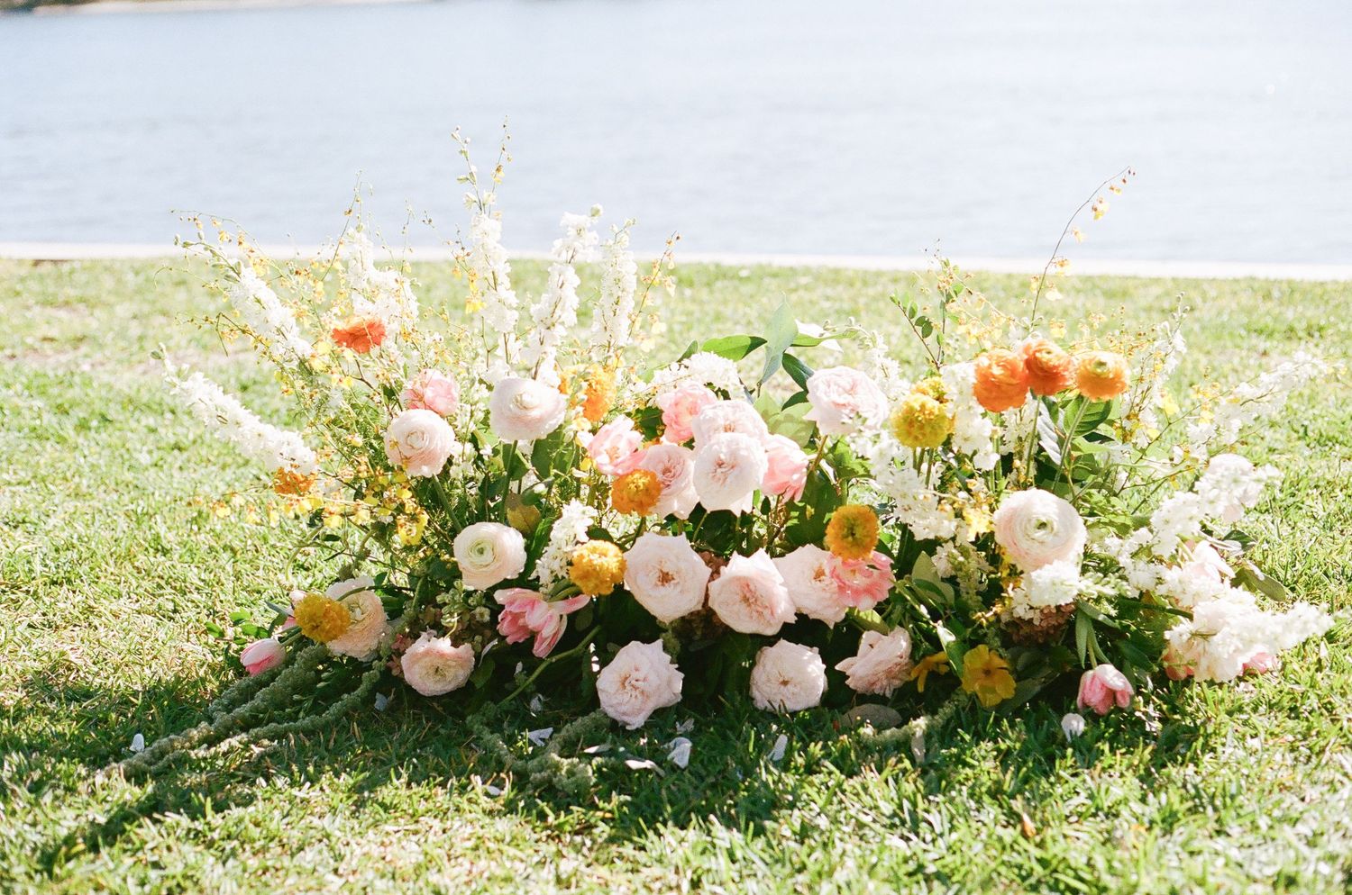 Romantic peach and white floral arrangements line the ground creating a beautiful outdoor wedding aisle.