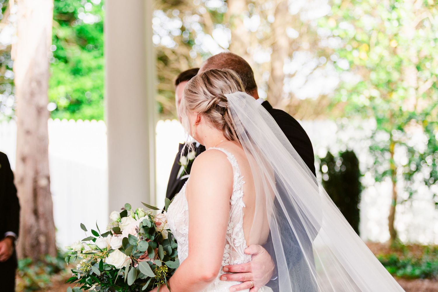 A bride and groom share an intimate moment under a white gazebo surrounded by lush greenery.