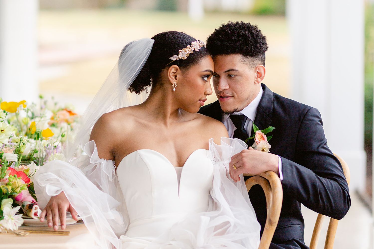 A tender wedding moment between a couple with a floral arrangement of daisies and wildflowers in the background.