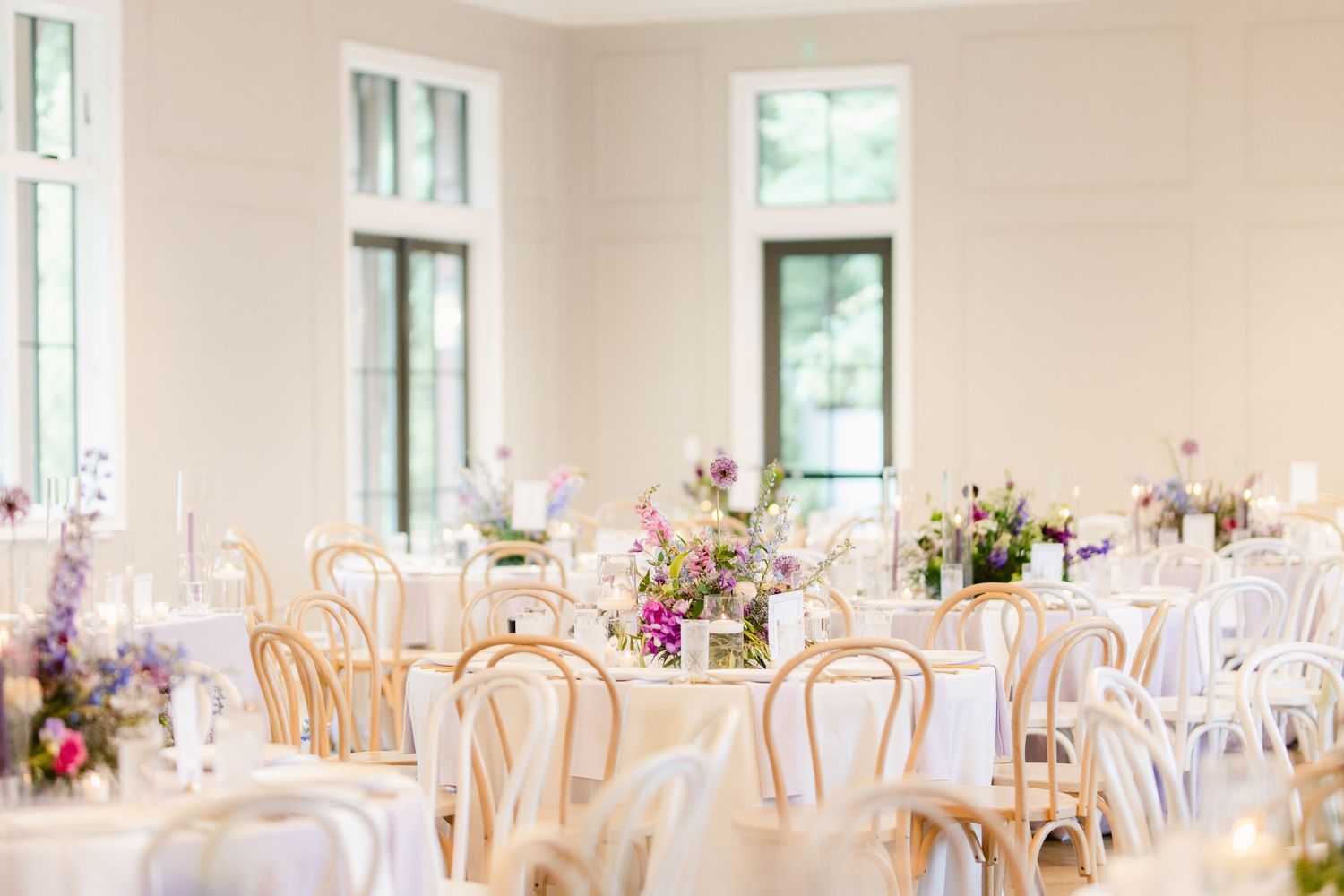 An elegant wedding reception venue with round tables, white linens, gold chairs and pink floral centerpieces.