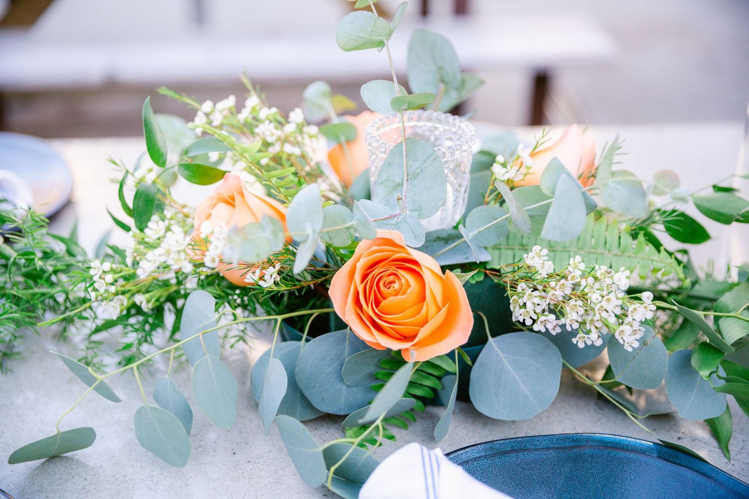Elegant wedding floral arrangements featuring peach roses, white flowers, and eucalyptus greenery on a light blue backdrop.