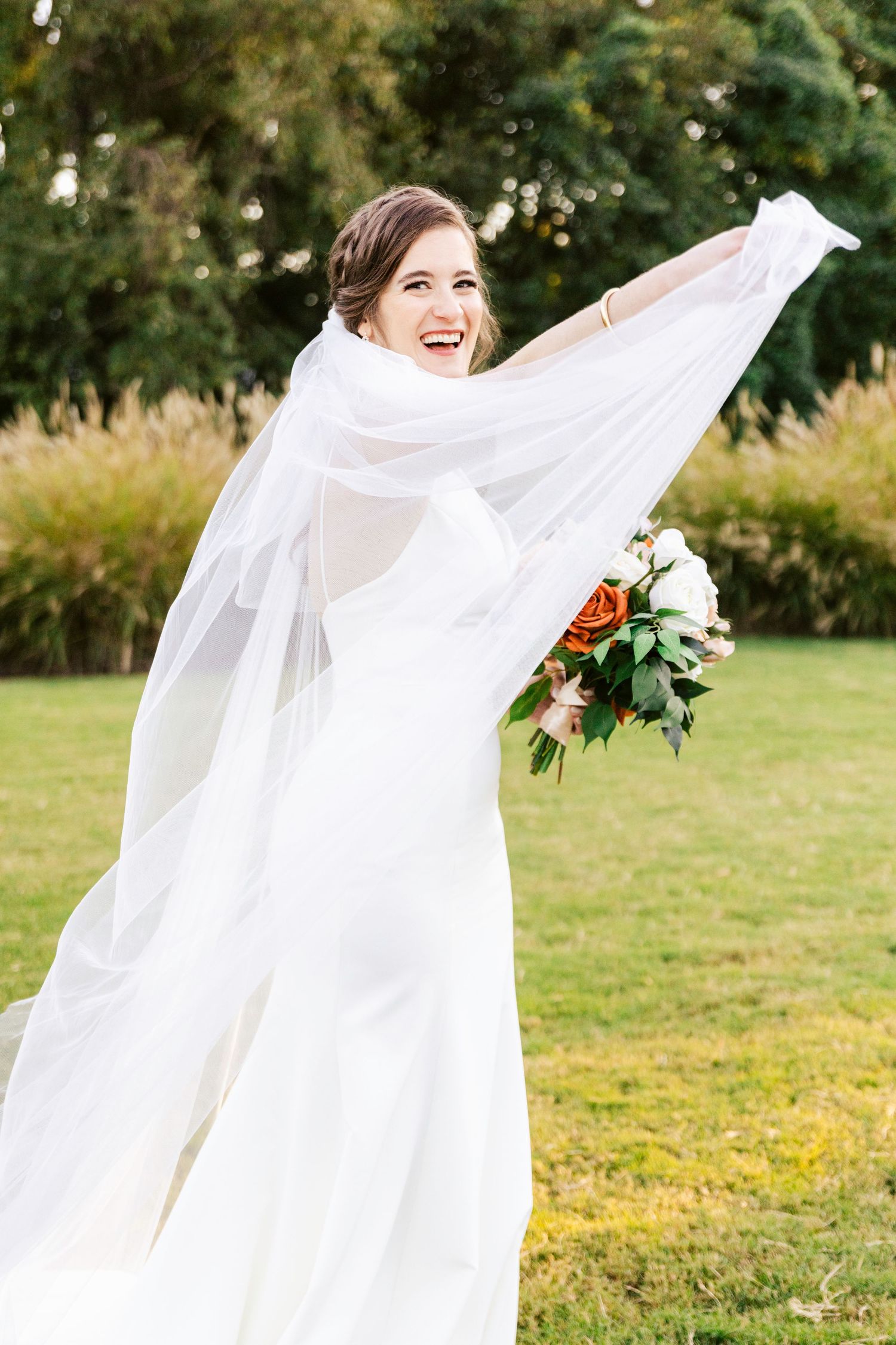 Bride twirling in flowing white wedding dress outdoors in natural setting.