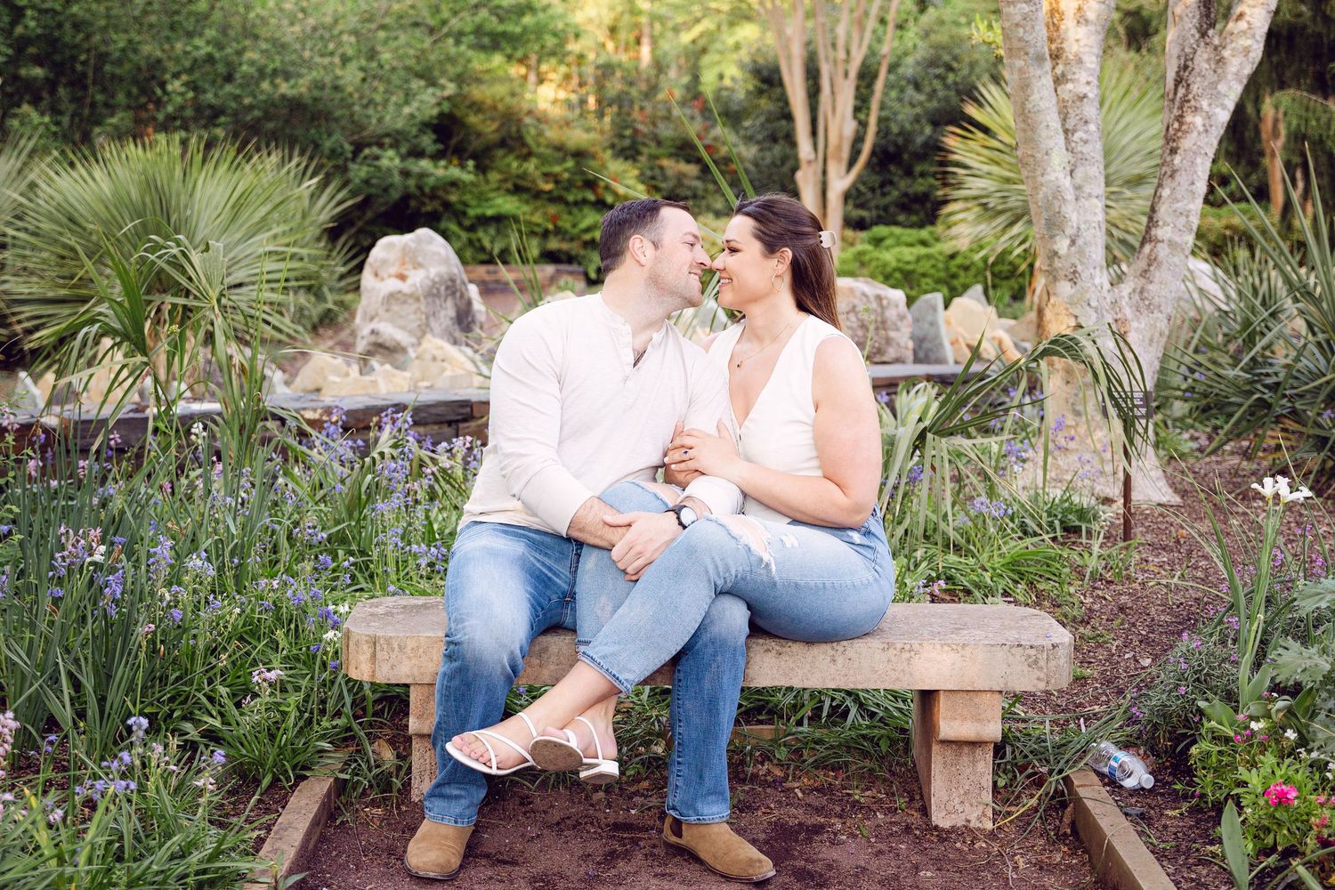 Engagement photos on rustic wooden bench surrounded by tropical garden landscaping.