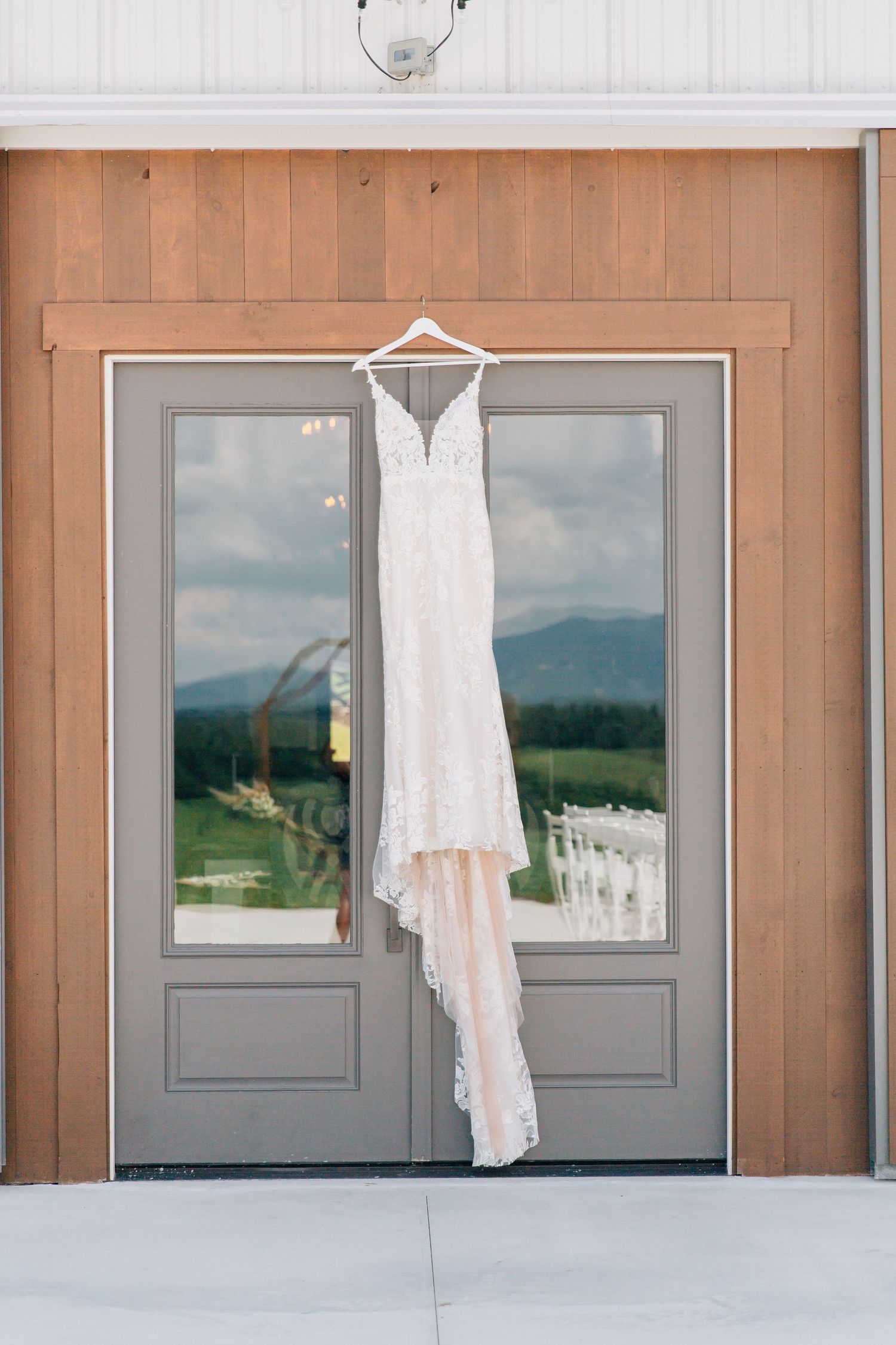 Elegant white lace wedding dress hanging against wooden doors with mountain views.