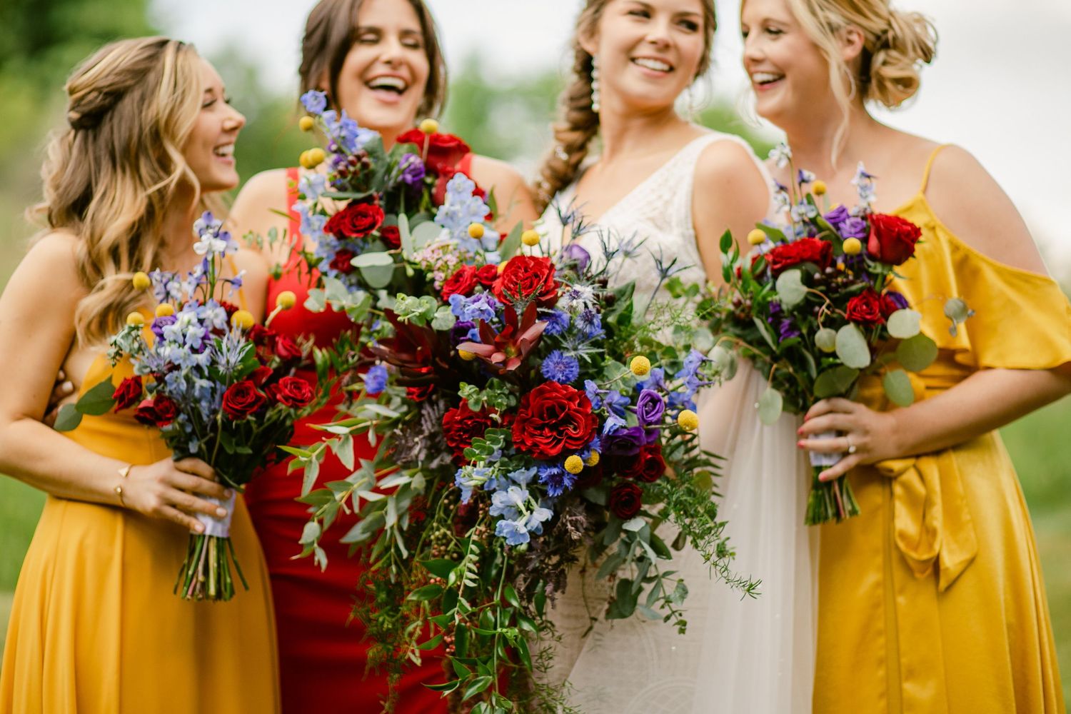 Bridesmaids in yellow dresses holding vibrant red and blue floral bouquets.