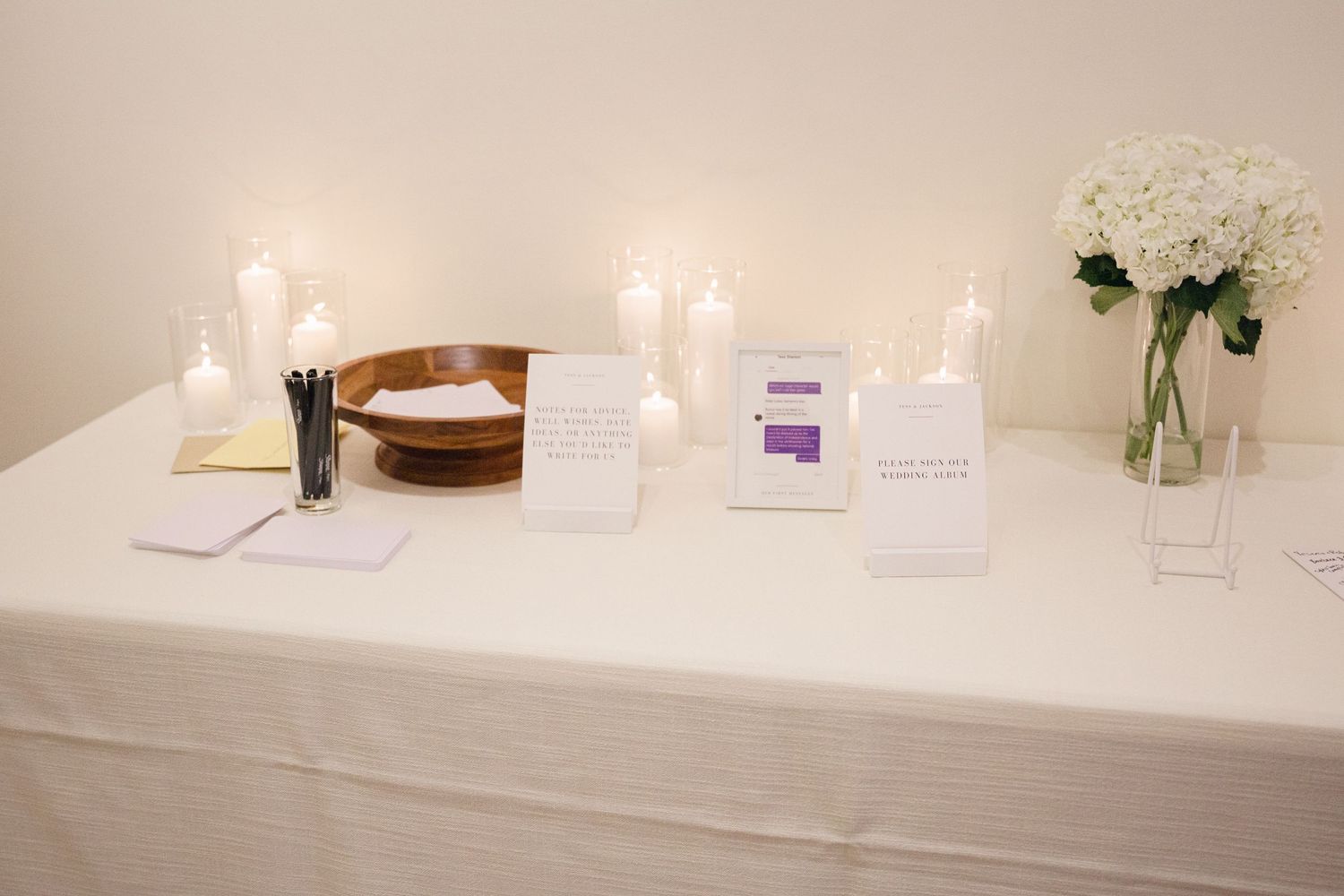 White covered reception table with various signs and accents for a wedding.