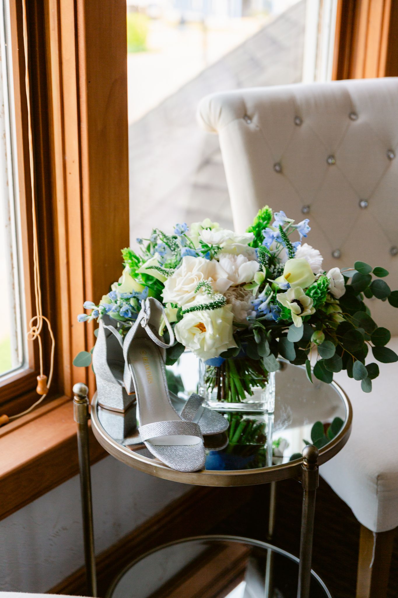 White floral arrangements in elegant vases line a windowsill with natural light streaming through wooden window frames.