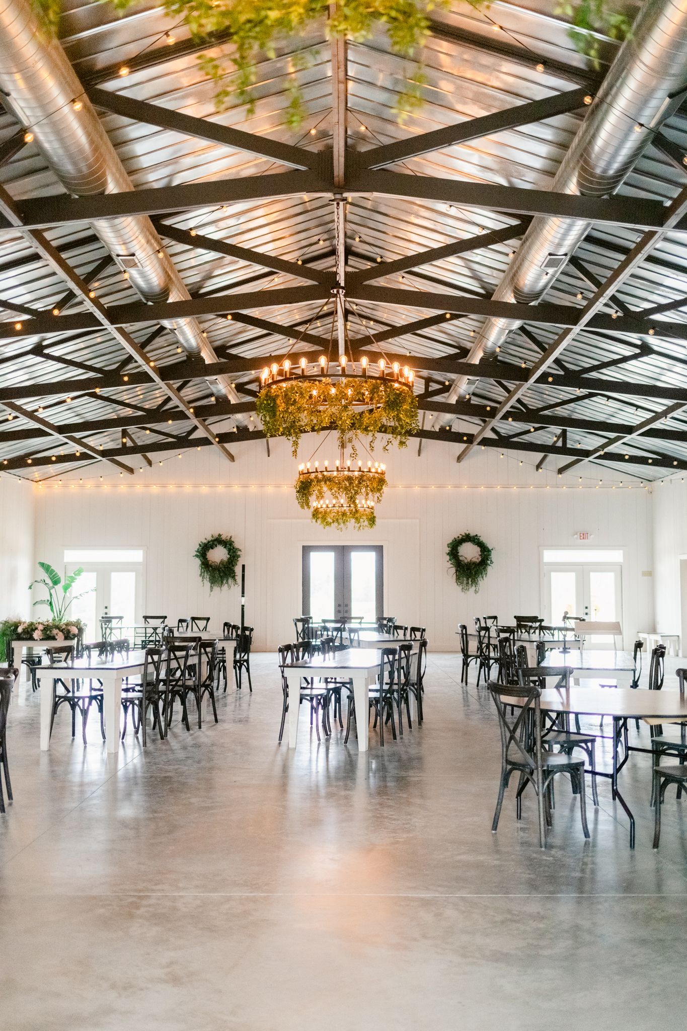 Large open event venue with exposed wood beams, elegant chandeliers, and modern black chairs set up for a gathering.