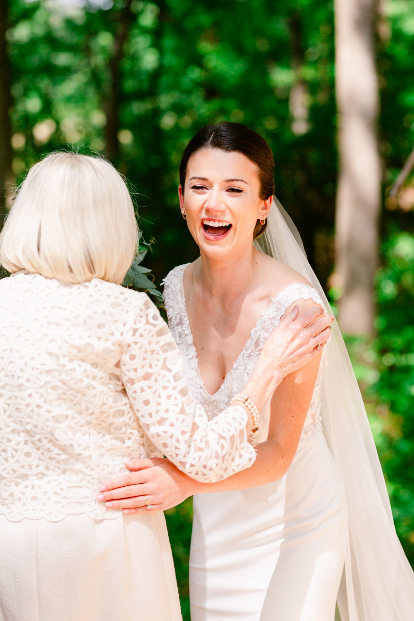 A joyful moment shared between a bride in a white gown and veil with an older woman in a lace dress outdoors.
