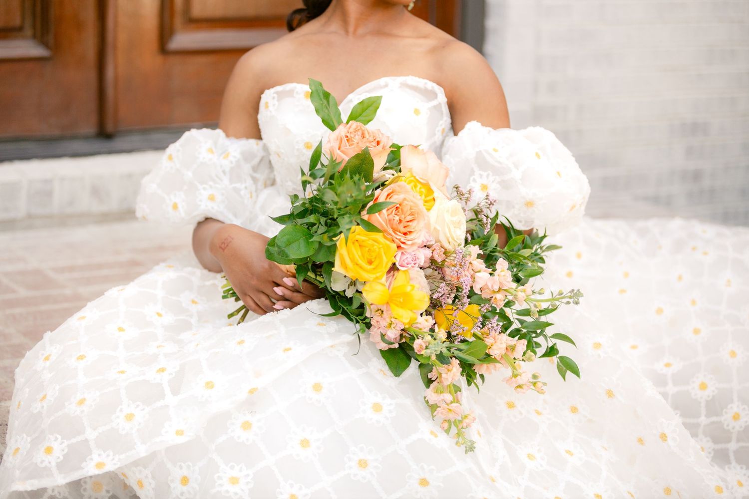 A beautiful bridal bouquet with yellow and peach flowers against a white lace wedding dress.