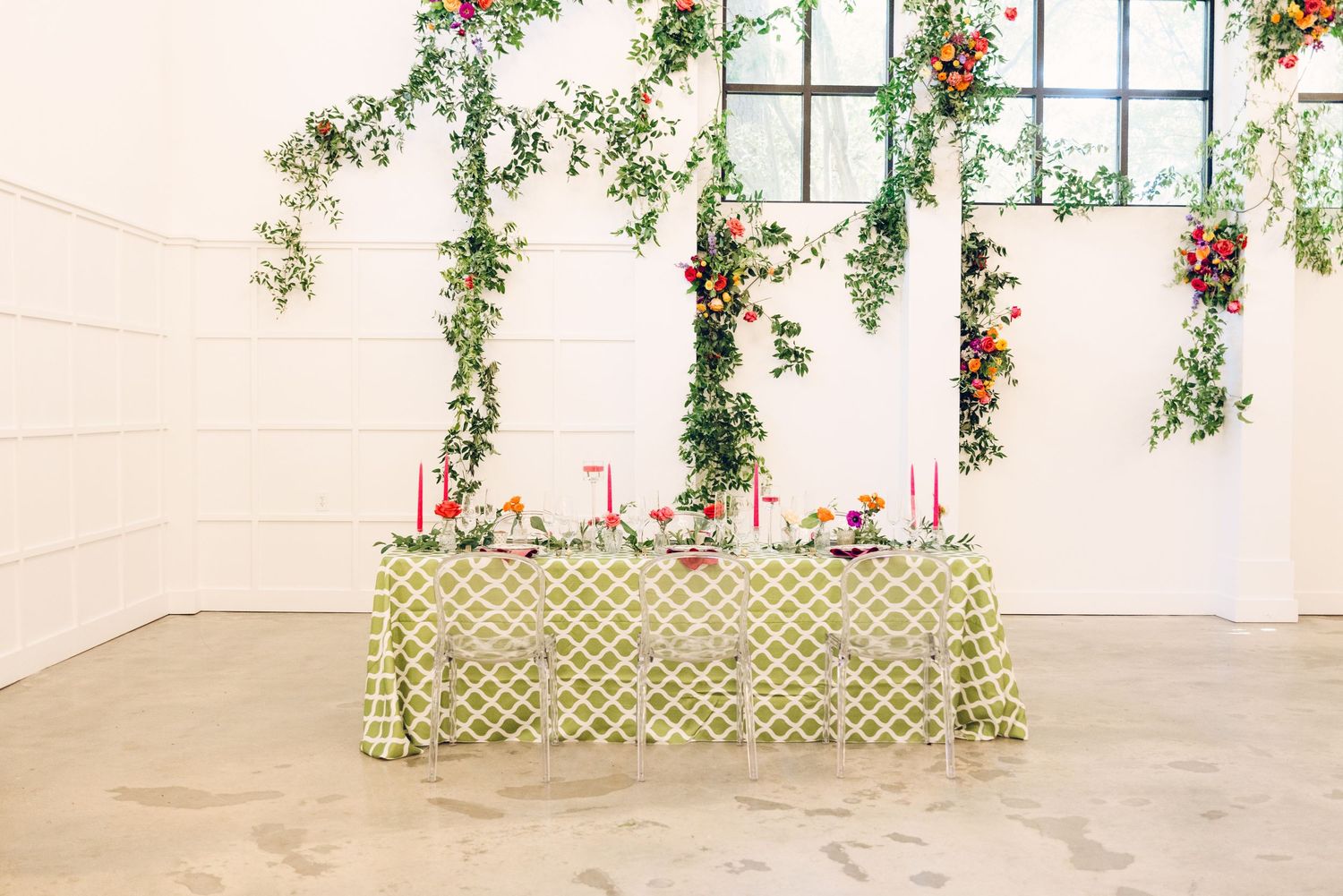 Bright floral arrangements and hanging greenery adorn a modern white event space.