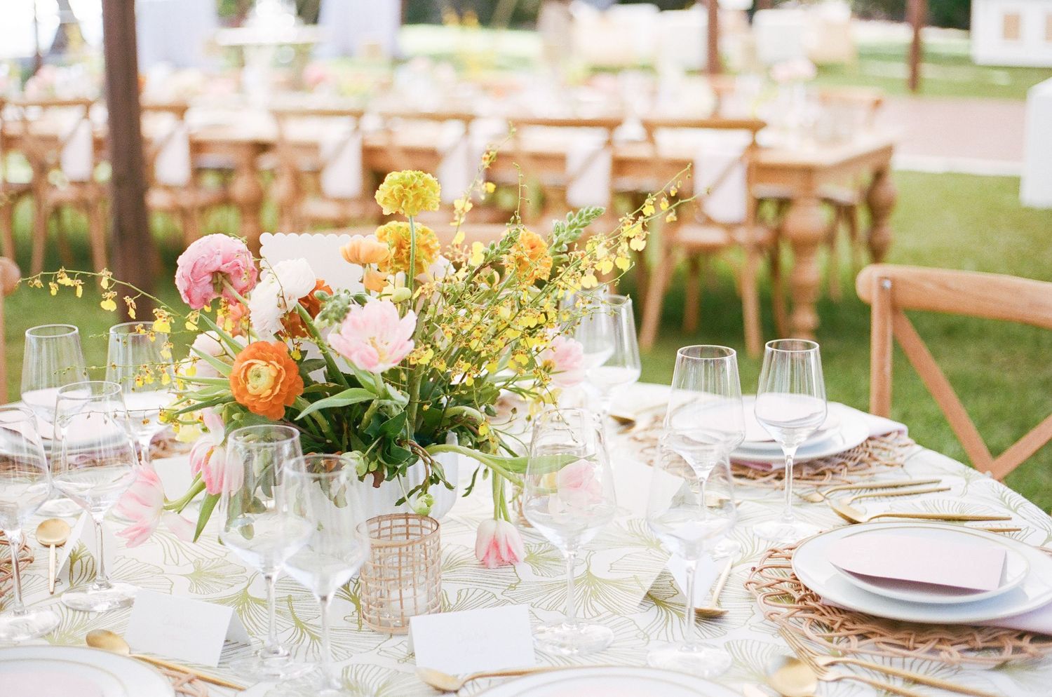 Elegant outdoor wedding reception table settings with floral centerpieces and glassware on white tablecloths.