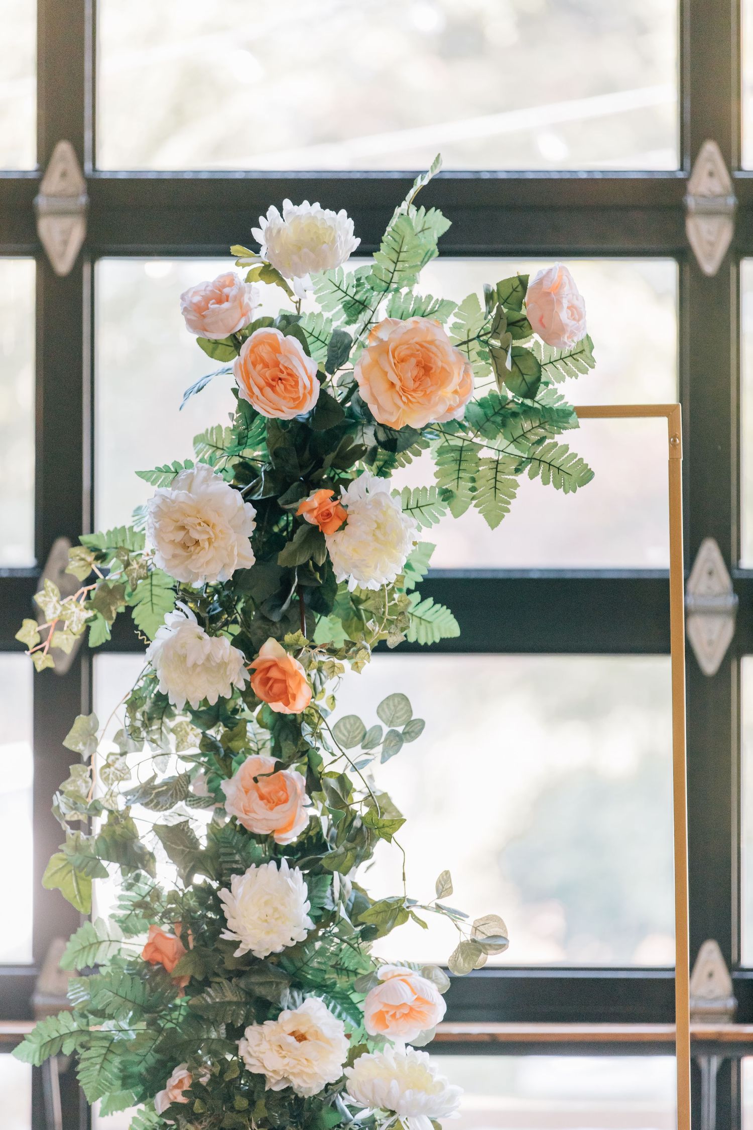 Elegant floral arch with peach and white roses adorns a window frame in an indoor setting.