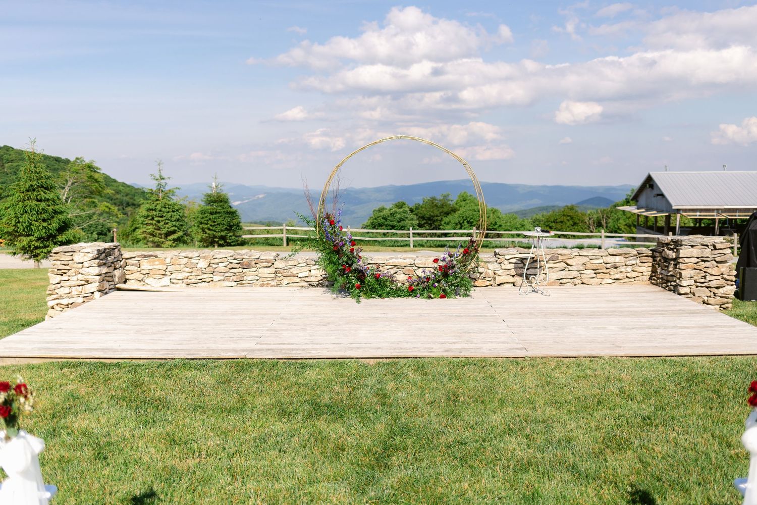 Outdoor wedding ceremony space with stone platform and circular floral arch against mountain backdrop.